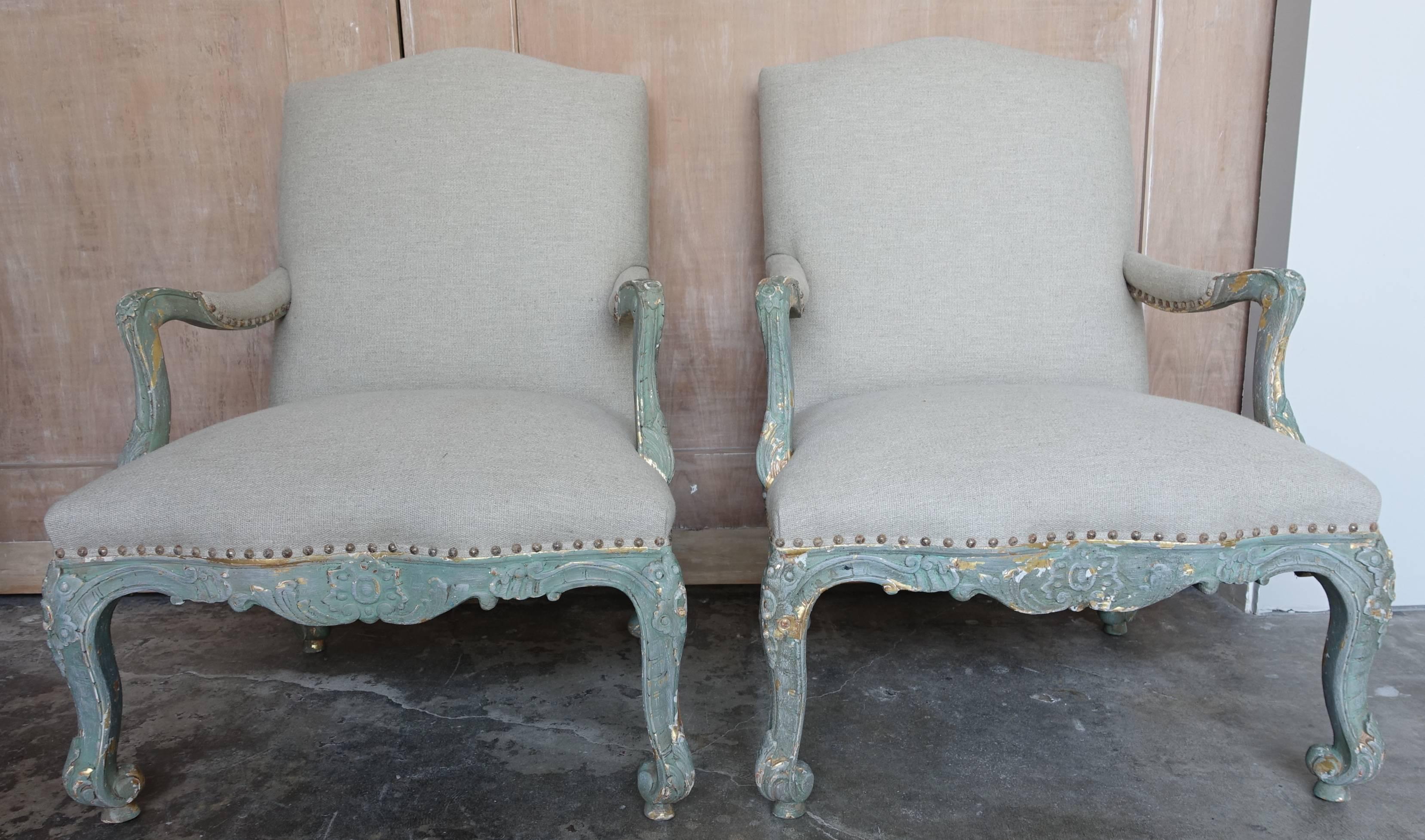 Pair of French aqua painted and 22-karat giltwood carved fauteuils standing on four slight cabriole legs. Newly upholstered in natural grain colored linen with elegant arched back and antiqued nail head trim detail.