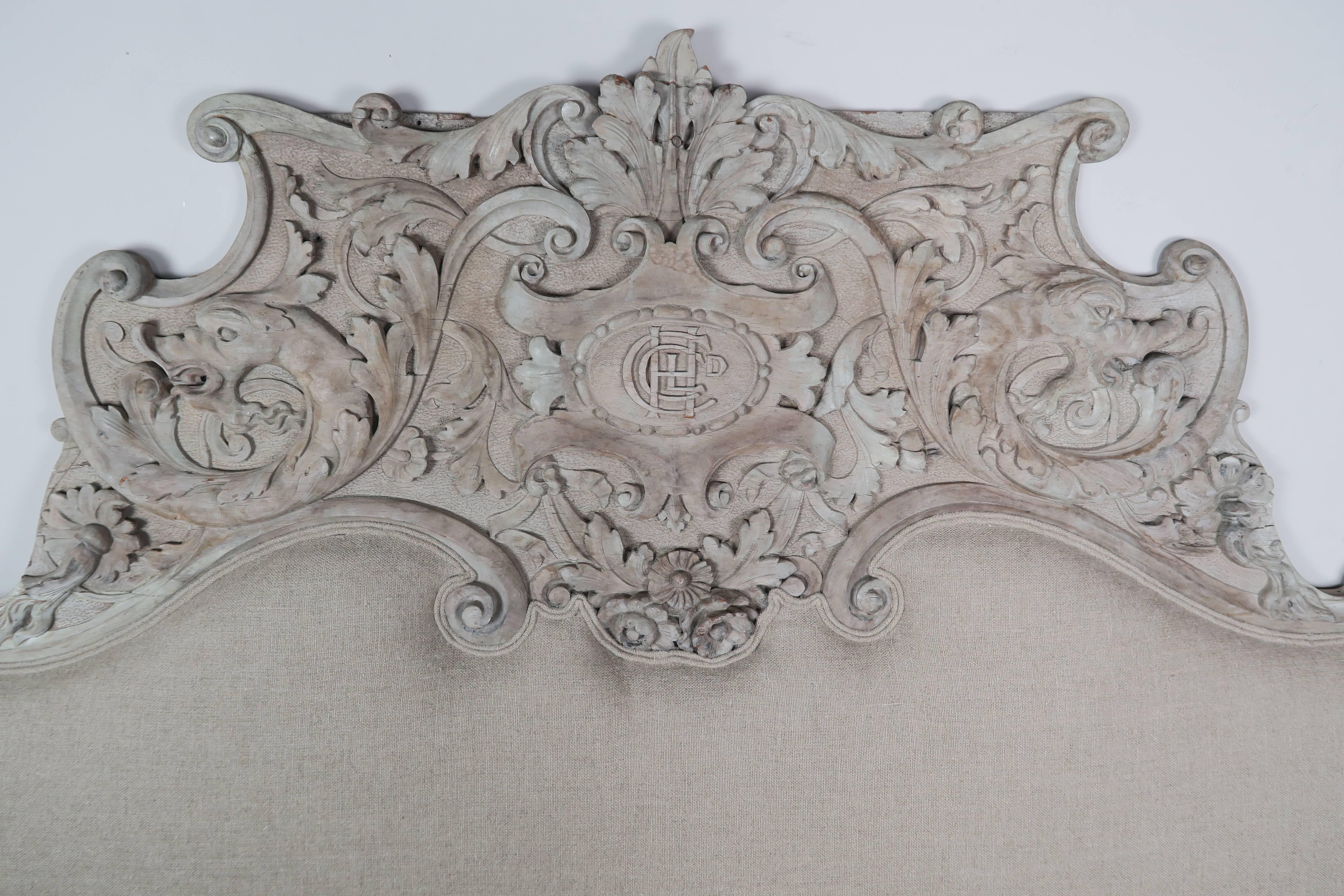 19th century, Italian carved Rococo carved headboard upholstered in a natural washed Belgium linen. The carving has dolphins and swirling acanthus leaves with a center monogrammed cartouche. Accommodates a king size mattress.