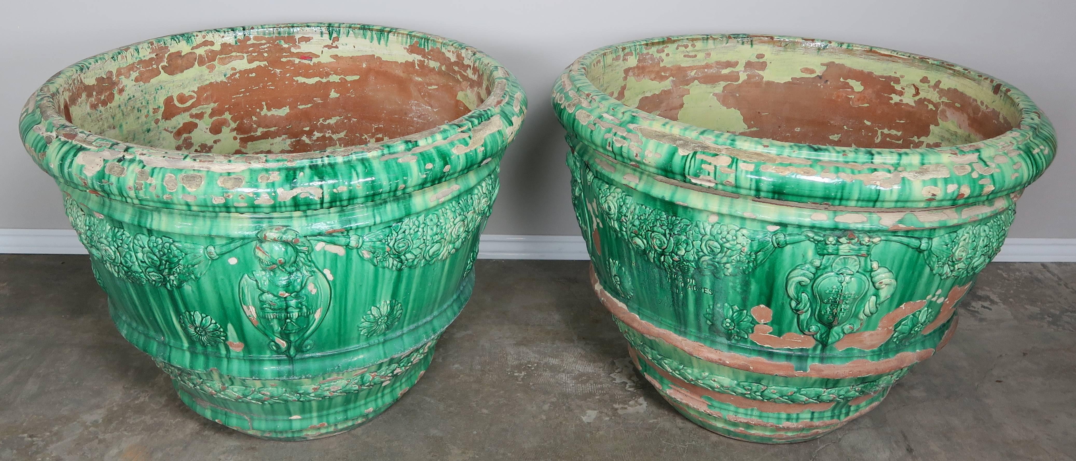 A pair of large green glazed Italian terra cotta planters with raised details depicting a Knight, crown and floral arrangements throughout. Smooth wide lip. Inscription denoting Firenze Italia.
