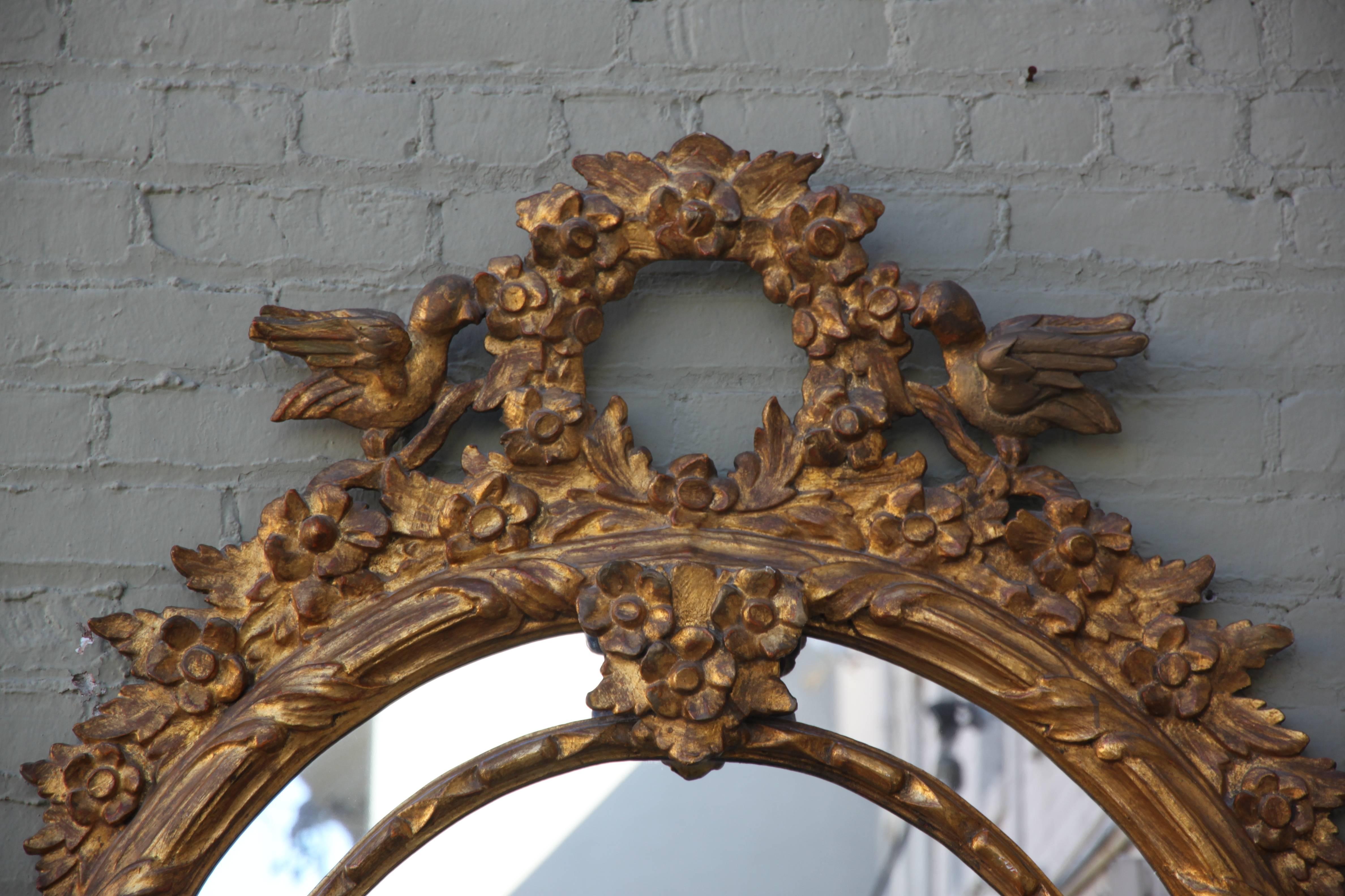French Louis XV style oval giltwood mirror with birds flanking a floral wreath.