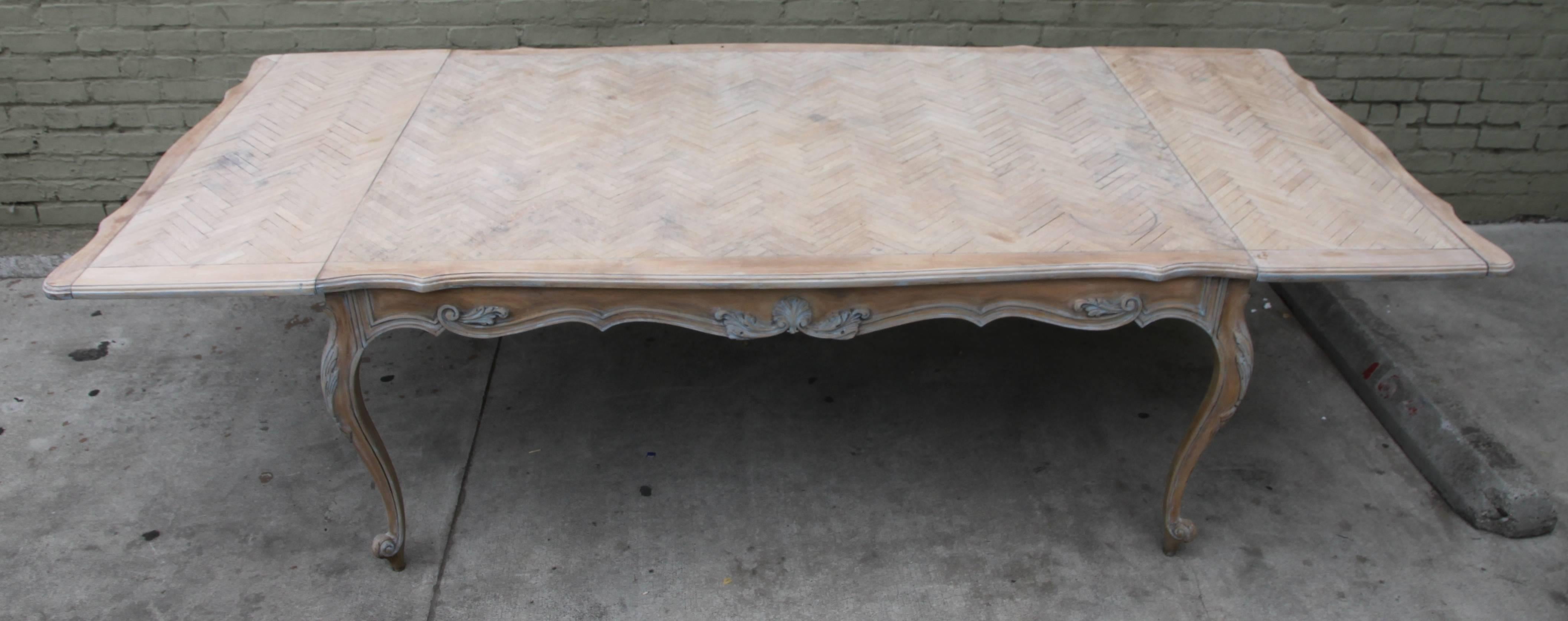 French parcel painted Louis XV style dining table with carved shell and acanthus leaf detailing. Parquetry top. Size of table including leaves: 111