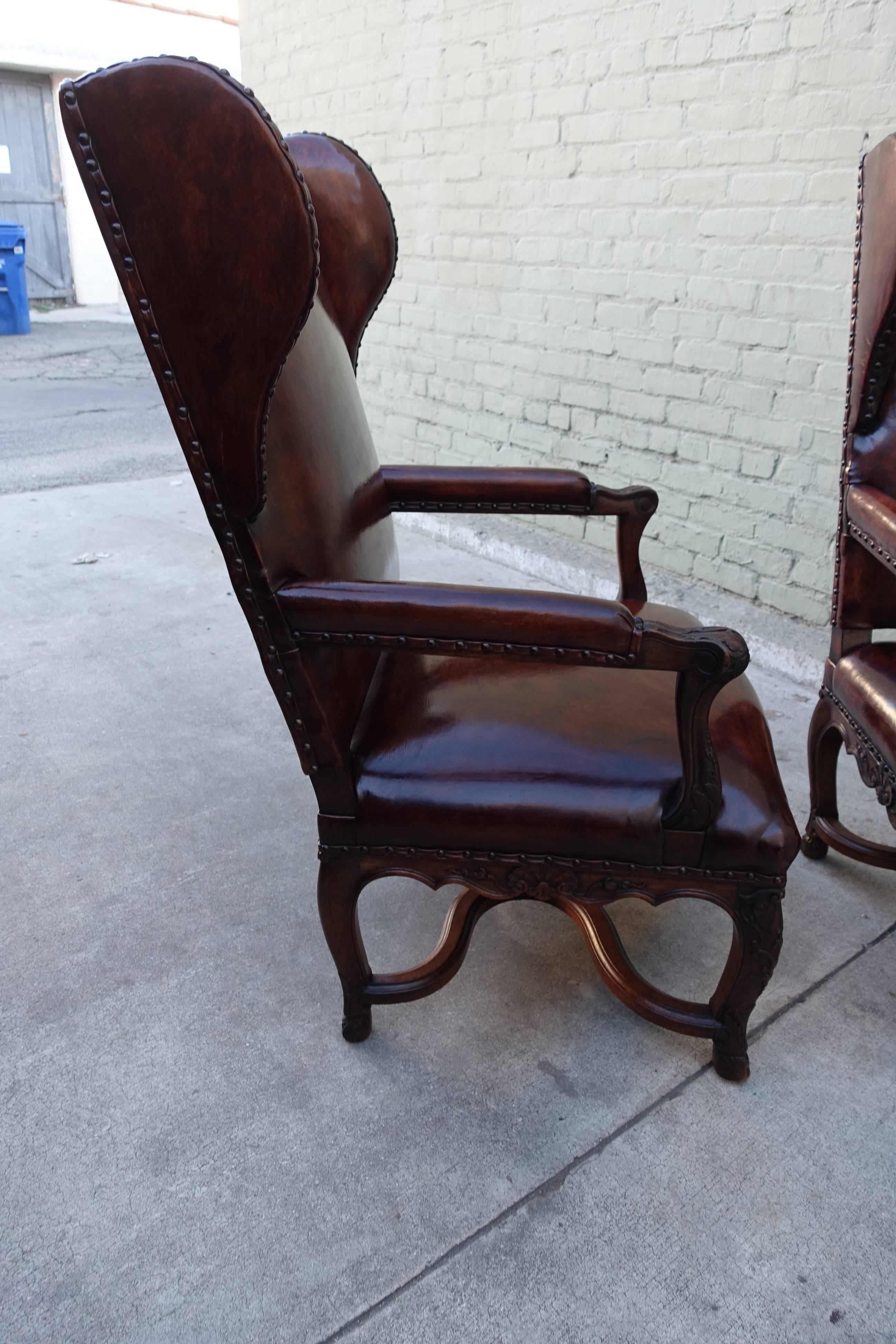 Pair of handsome Regence style rich leather upholstered French wing-back armchairs with nailhead trim over flat welt detail. The chairs stand on four cabriole legs that meet at centre 