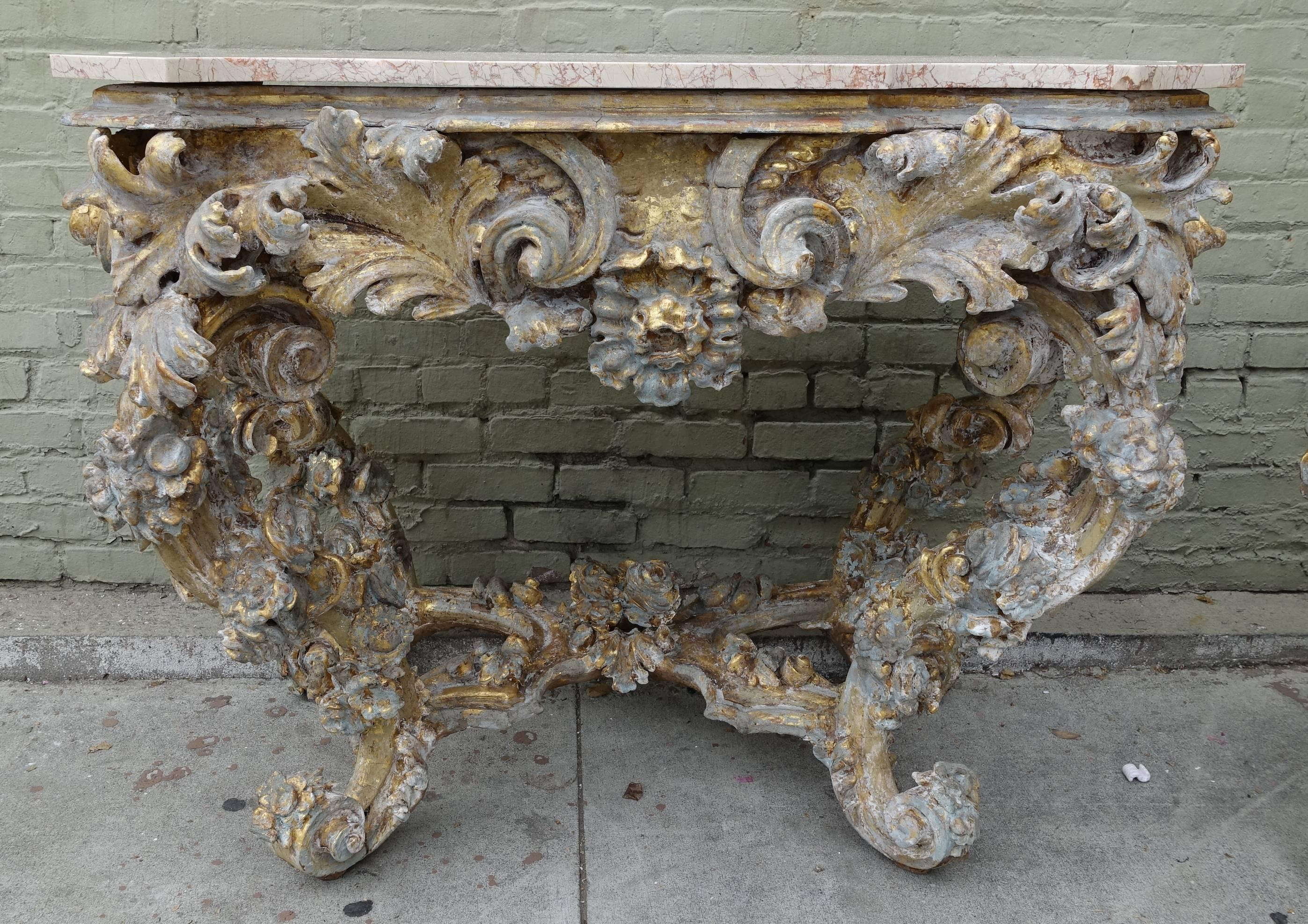 Pair of 19th century French Rococo style painted and giltwood consoles with cream rose serpentine shaped marble tops. The dramatic intricate carving on the consoles depicts scrolls, acanthus leaves and foliage throughout. Bottom 