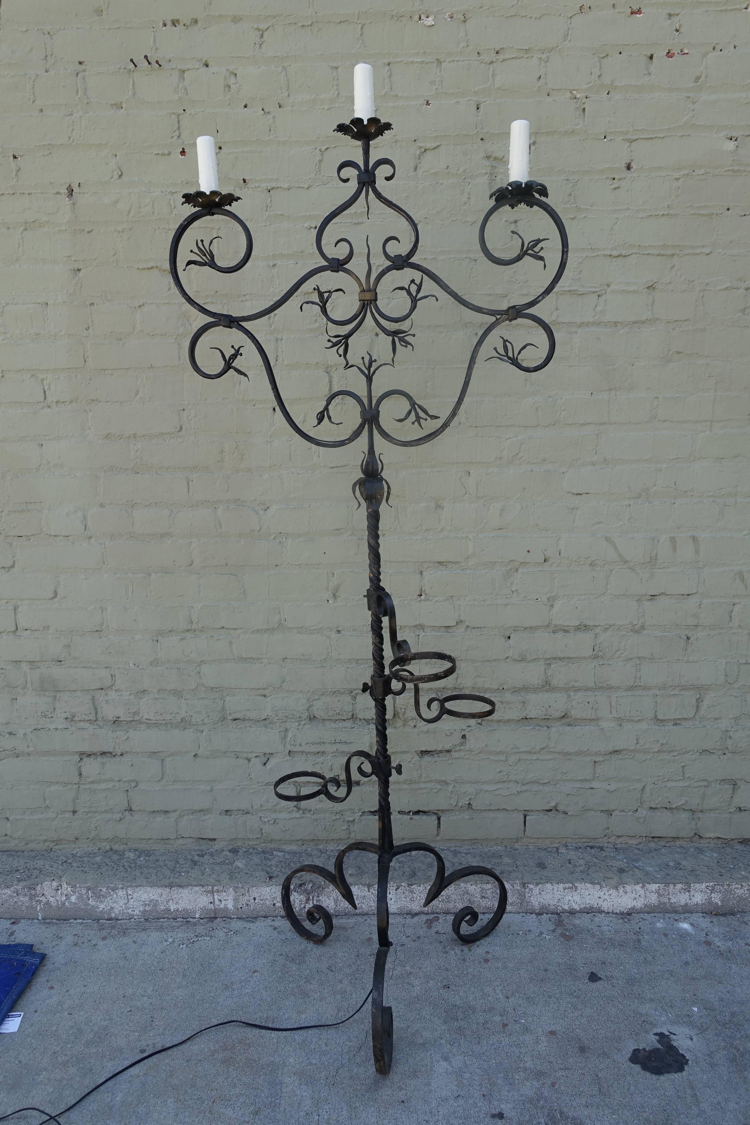 Spanish three-light wrought iron candelabra lamp that has been newly wired with drip wax candle covers. There are attachments for plants/candles/whatever. Beautiful forged iron detail throughout. Stands on a tripod scrolled base.