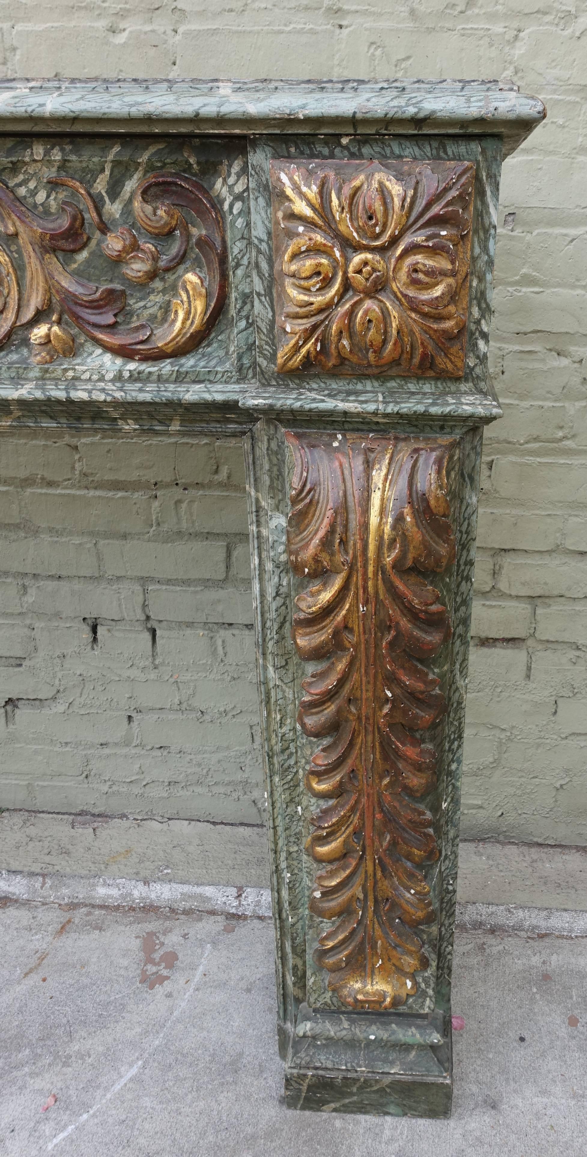 19th century Italian carved and giltwood faux marble fireplace mantel. Detailed with a center urn with swirling flowers and acanthus leaves throughout.