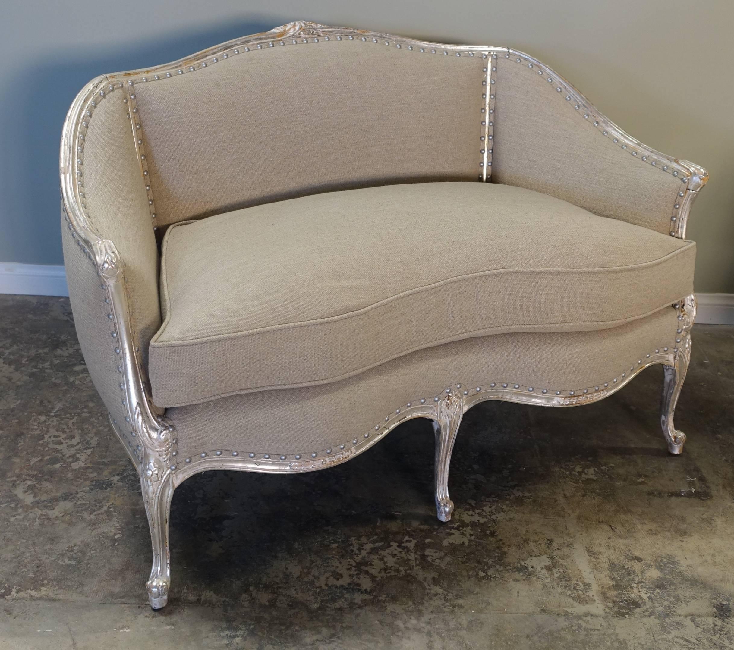 Pair of French carved silvered Louis XV style settees standing on five cabriole legs with rams head feet. Newly upholstered in natural grain colored linen with down filled loose seat cushions. The cushion has a self-cord detail. The settee frame has