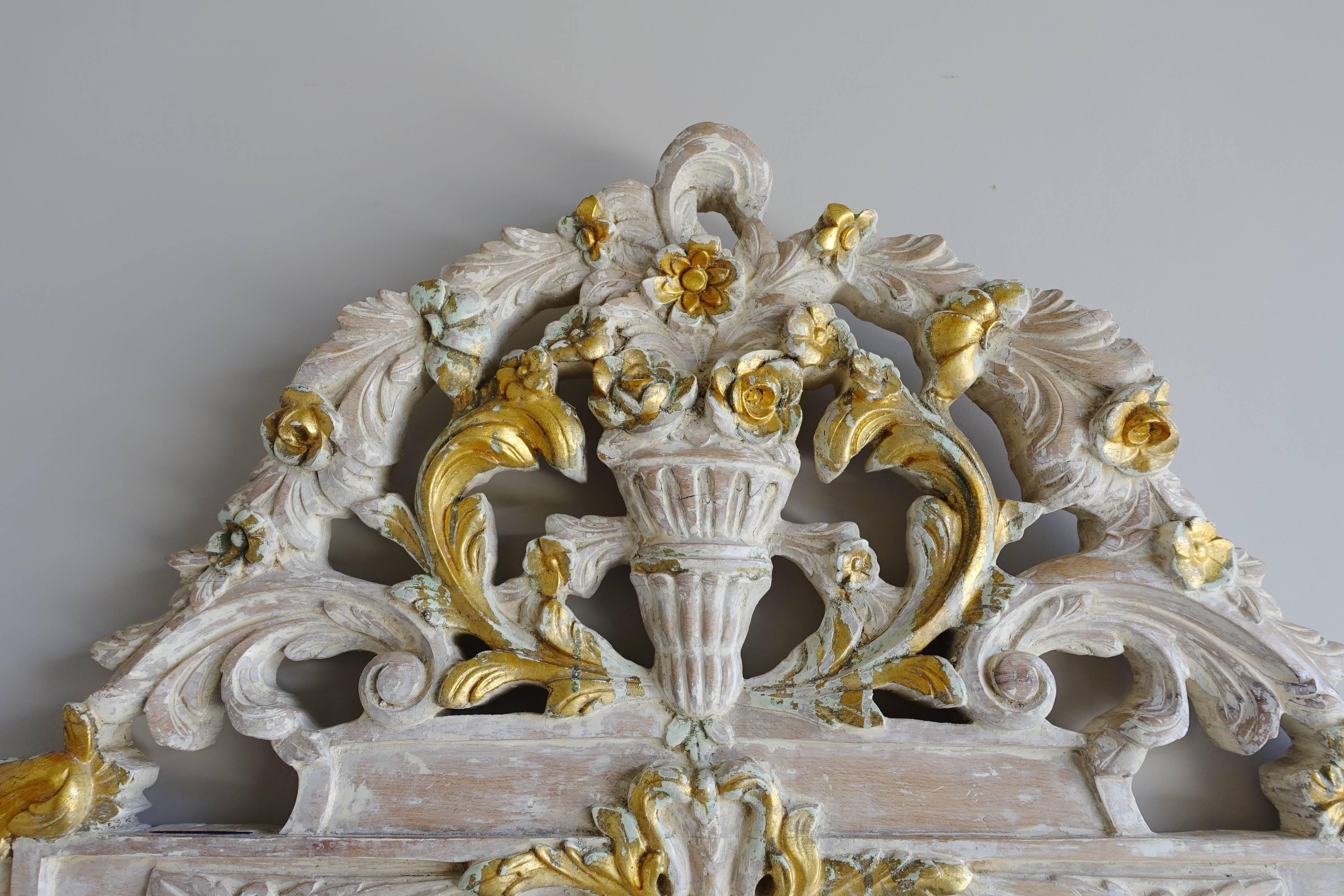French Rococo style hand-carved white washed and parcel-gilt headboard. The center urn of flowers is surrounded by garlands of flowers cascading down with delicate roses and acanthus leaves swirling throughout.