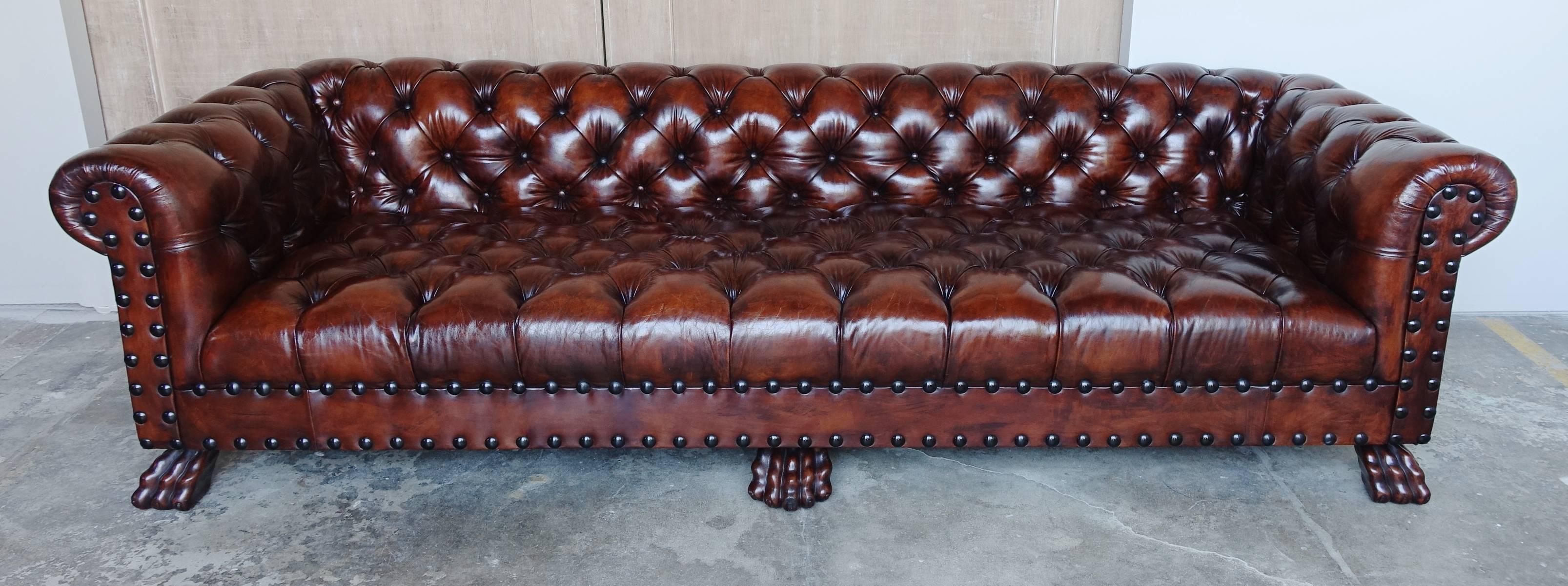 Monumental scaled leather tufted Chesterfield style sofa with double row of nailhead trim. This one-of-a-kind piece stands on six walnut finished carved wood feet. Beautiful rich patina.