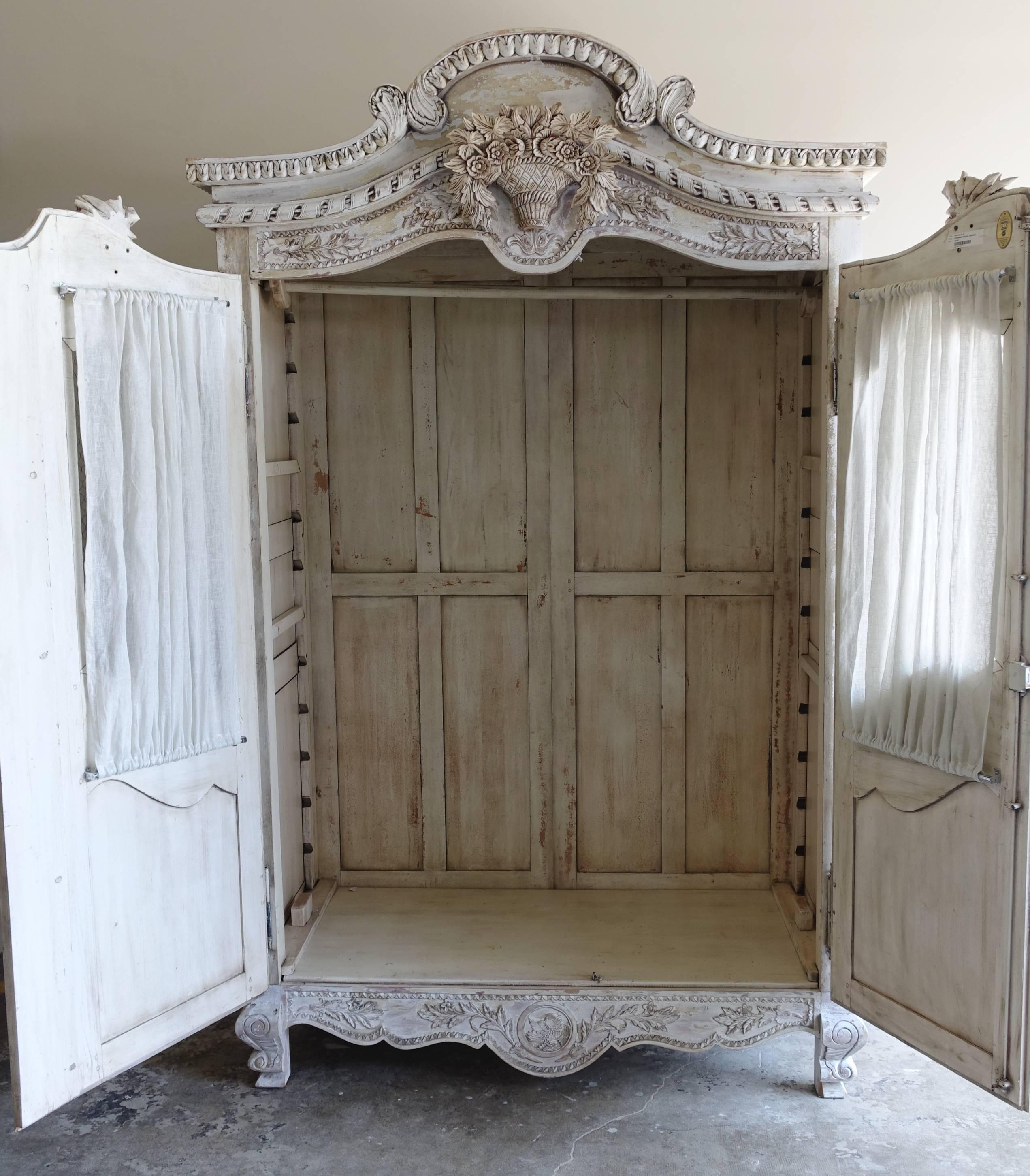 Antique wedding armoires were hand-carved by a father for his daughter and filled with linens and clothes to move with her once she had wed. This Louis XV style French armoire has a finely carved basket of flowers with garlands of roses cascading