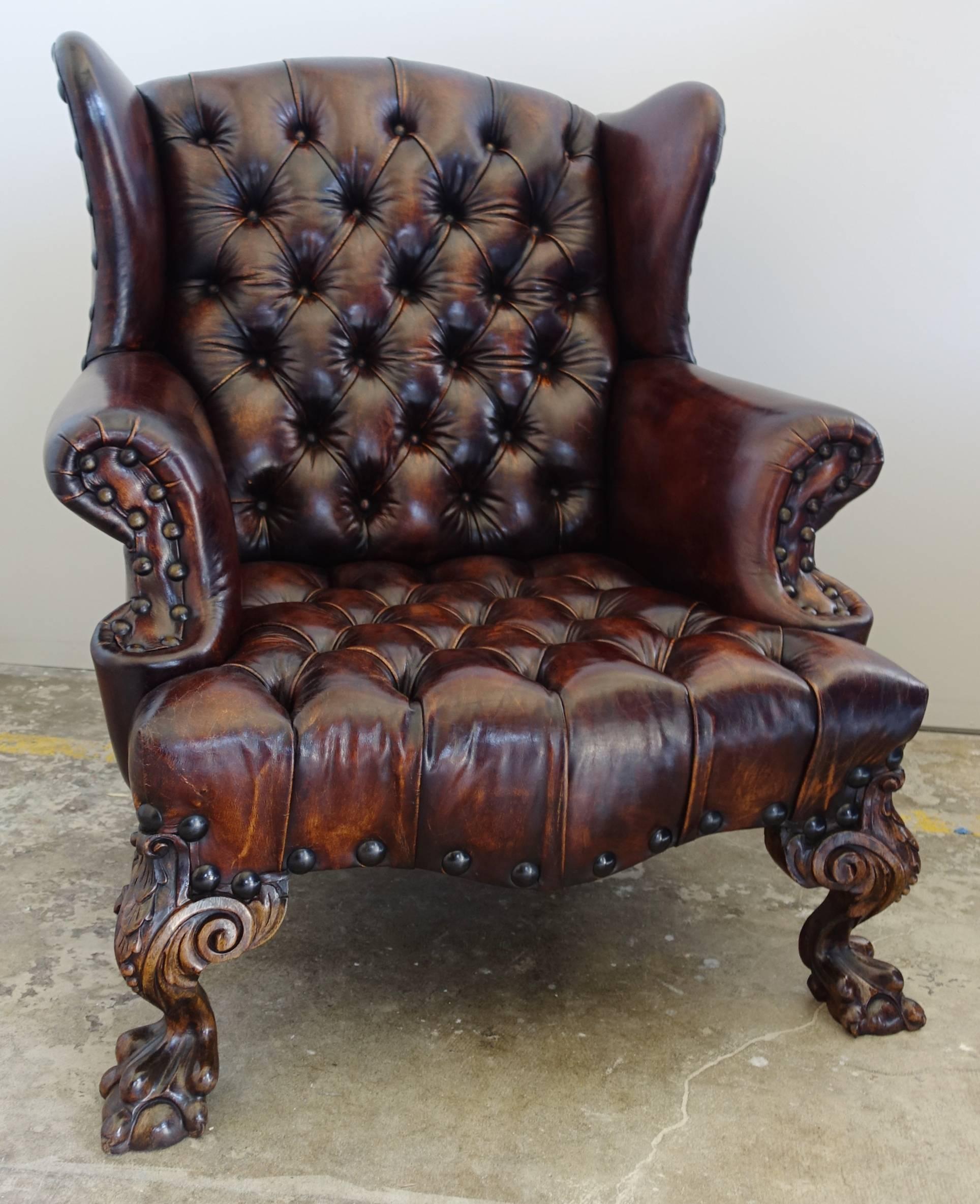Pair of early 1900s English Chippendale style tufted leather wingback chairs with nailhead trim detail. The armchairs stand on heavily carved walnut claw and ball feet in front. The cognac colored leather has distressing but remains in pristine