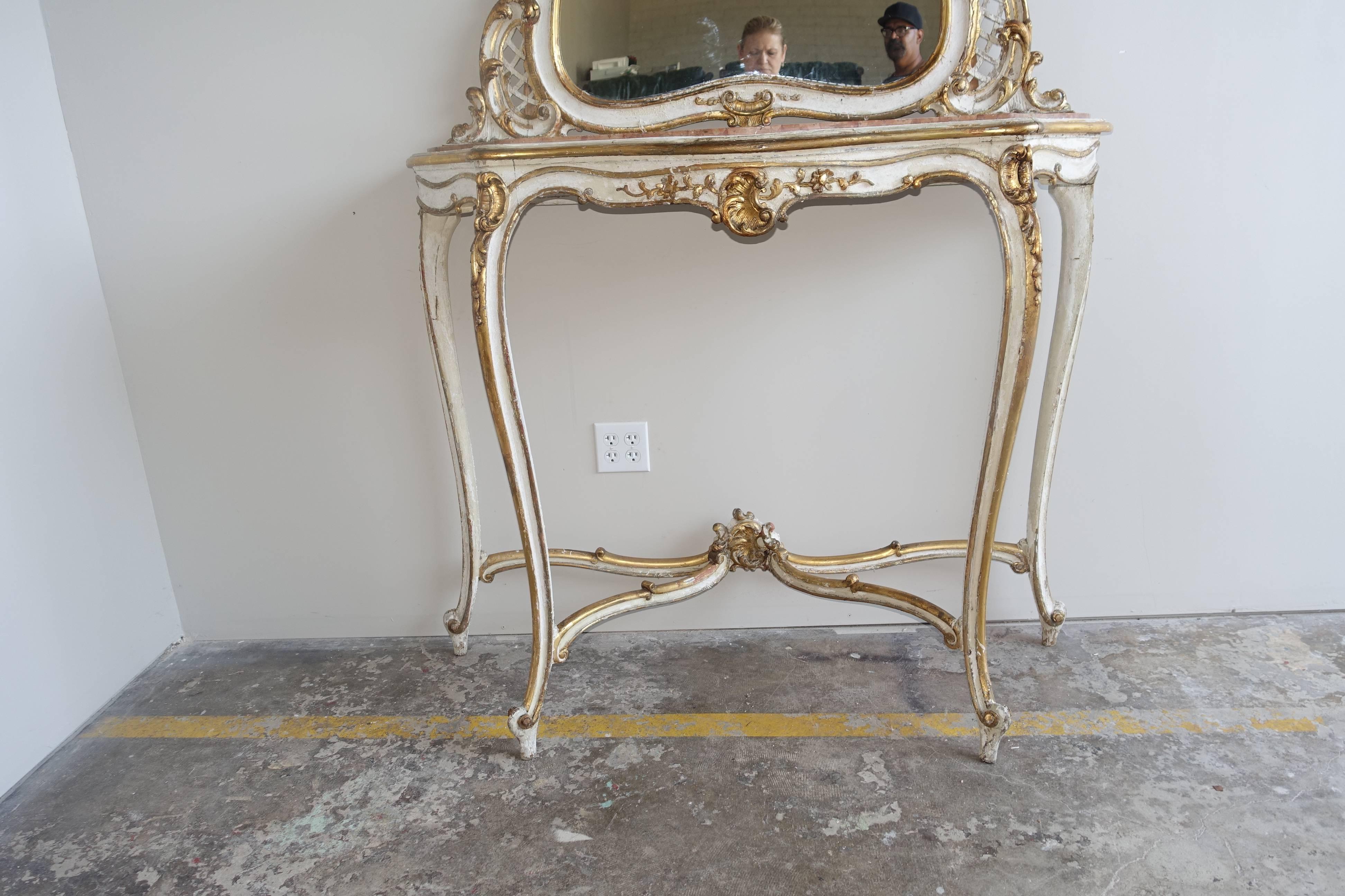 Louis XVI style painted and parcel-gilt console and mirror with original marble top. Console stands on four elegant cabriole legs with rams head feet. Bottom stretcher meets at center finial. Acanthus leaf detailing in 22-karat gold leaf finish.