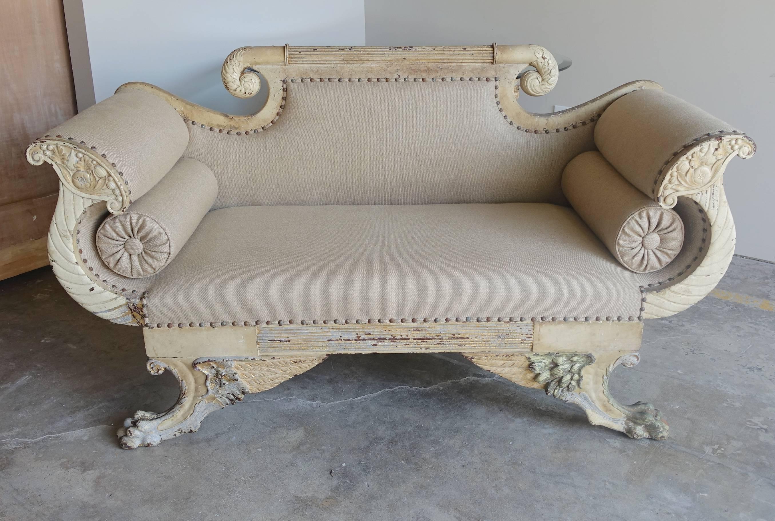 19th century Italian painted settee with two bolsters tucked under a pair of carved cornucopias. The settee stands on four winged lion's paw feet. Newly upholstered in Belgium Linen with spaced nailhead trim detail.