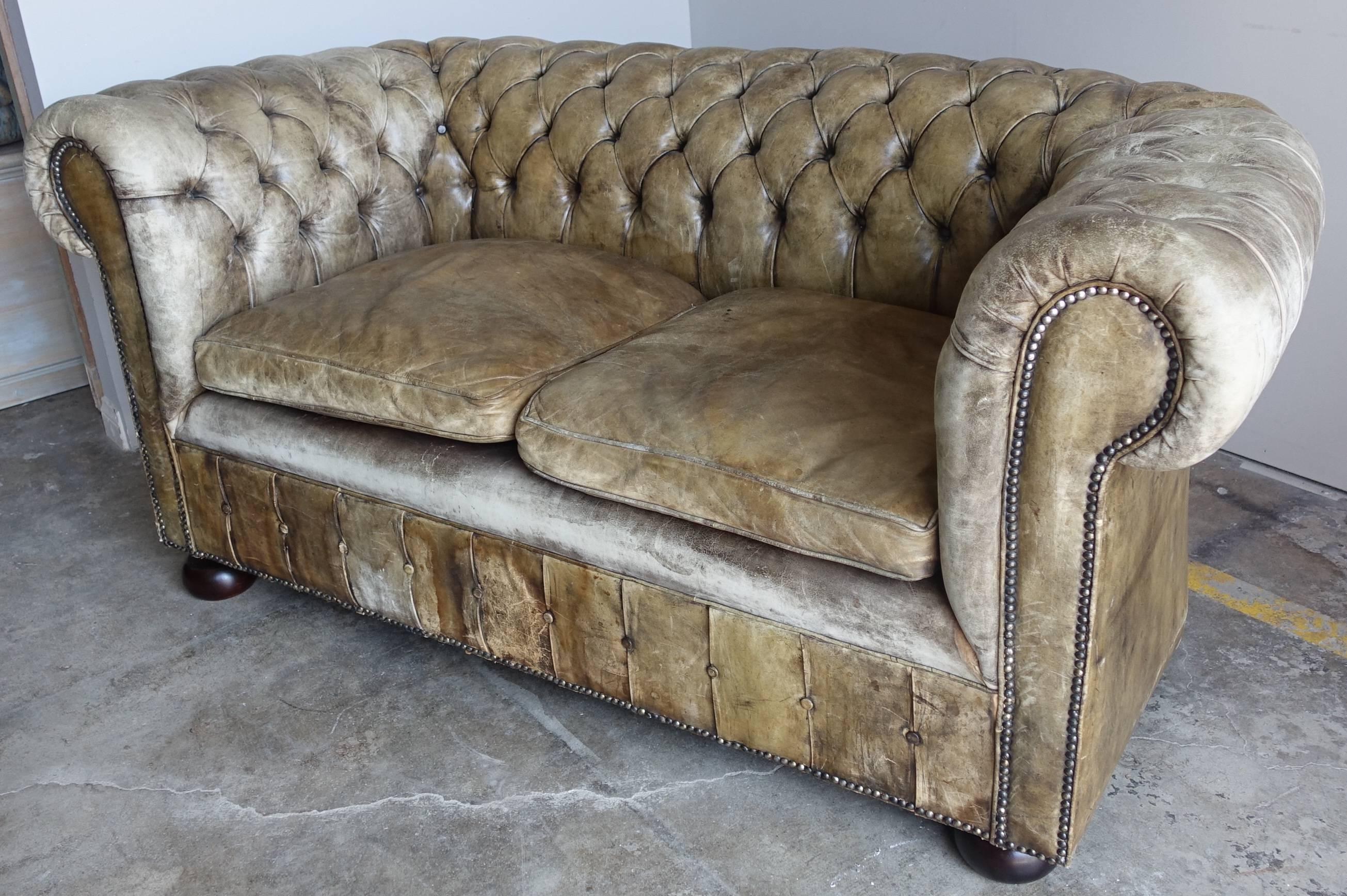 English wonderfully worn leather tufted Chesterfield sofa standing on bun feet with nailhead trim detail. Two loose seat cushions.
