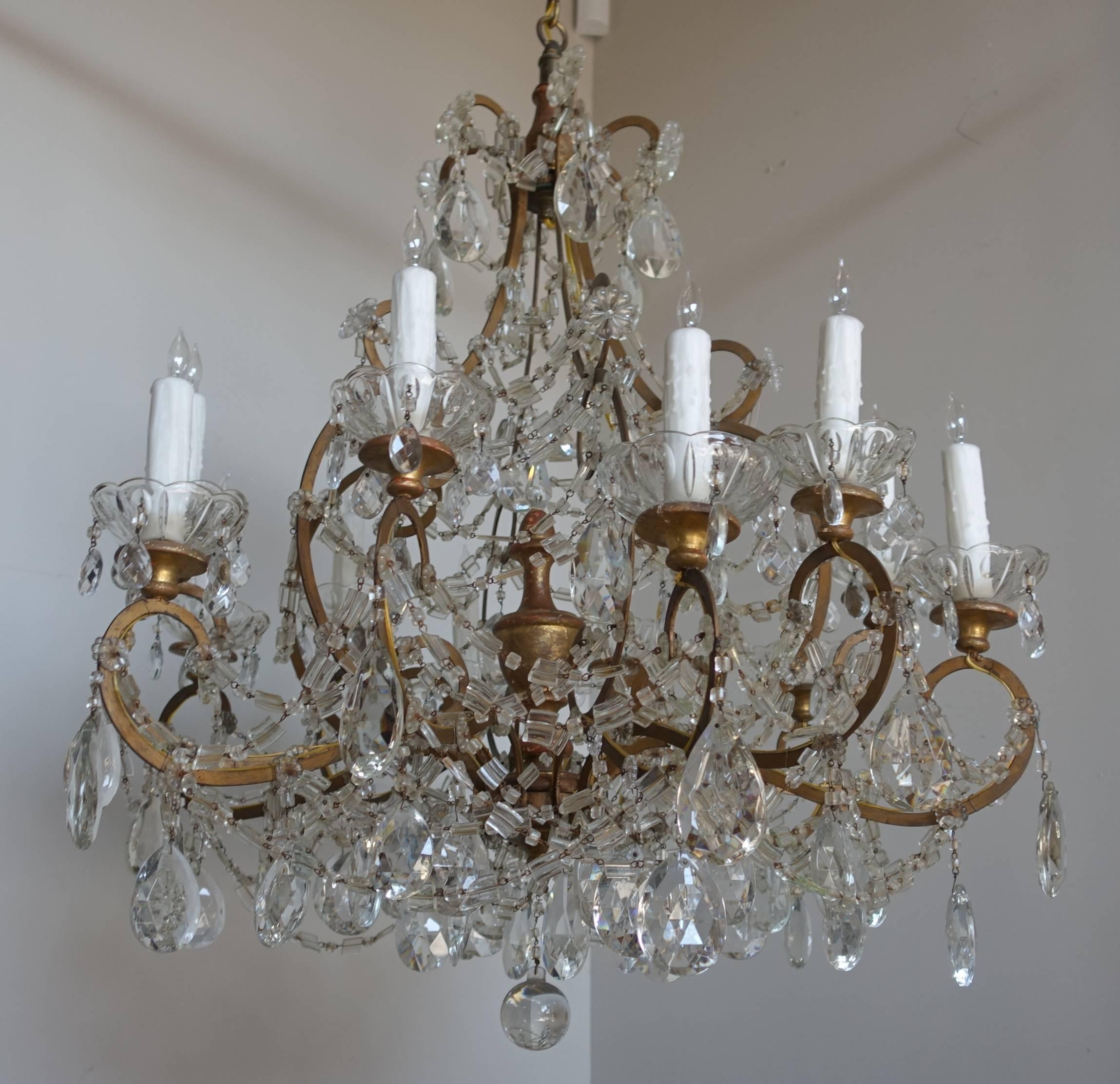 Twelve-light Italian gilt metal crystal chandelier with unique crystal garlands, crystal rosettes, and tear drop crystals throughout. Giltwood center finial and bobeches with crystal underneath. Rewired with new sockets and drip wax candle covers.