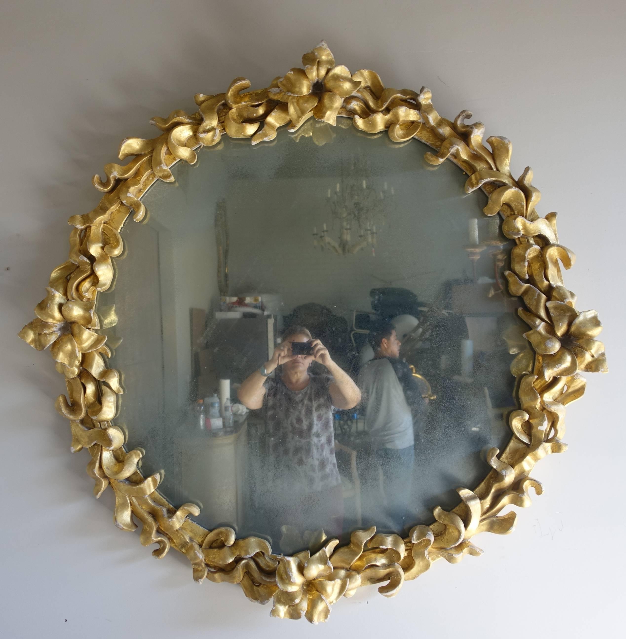 Hand-carved giltwood round mirror with leaves and flowers carved around the perimeter of the mirror frame. Antiqued mirror.