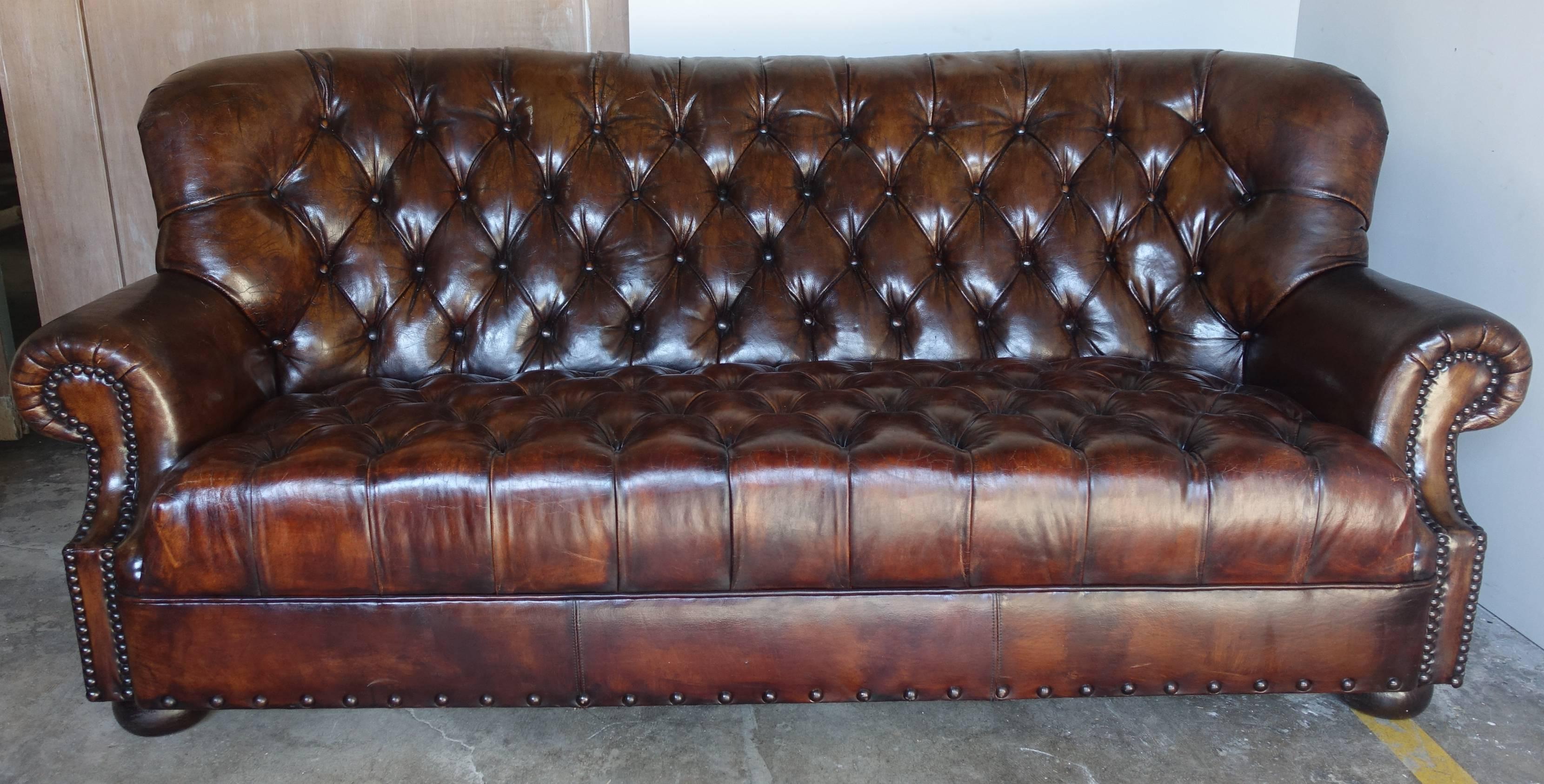 English leather tufted rolled arm sofa with nailhead trim detail. The sofa stands on four bun style feet.
