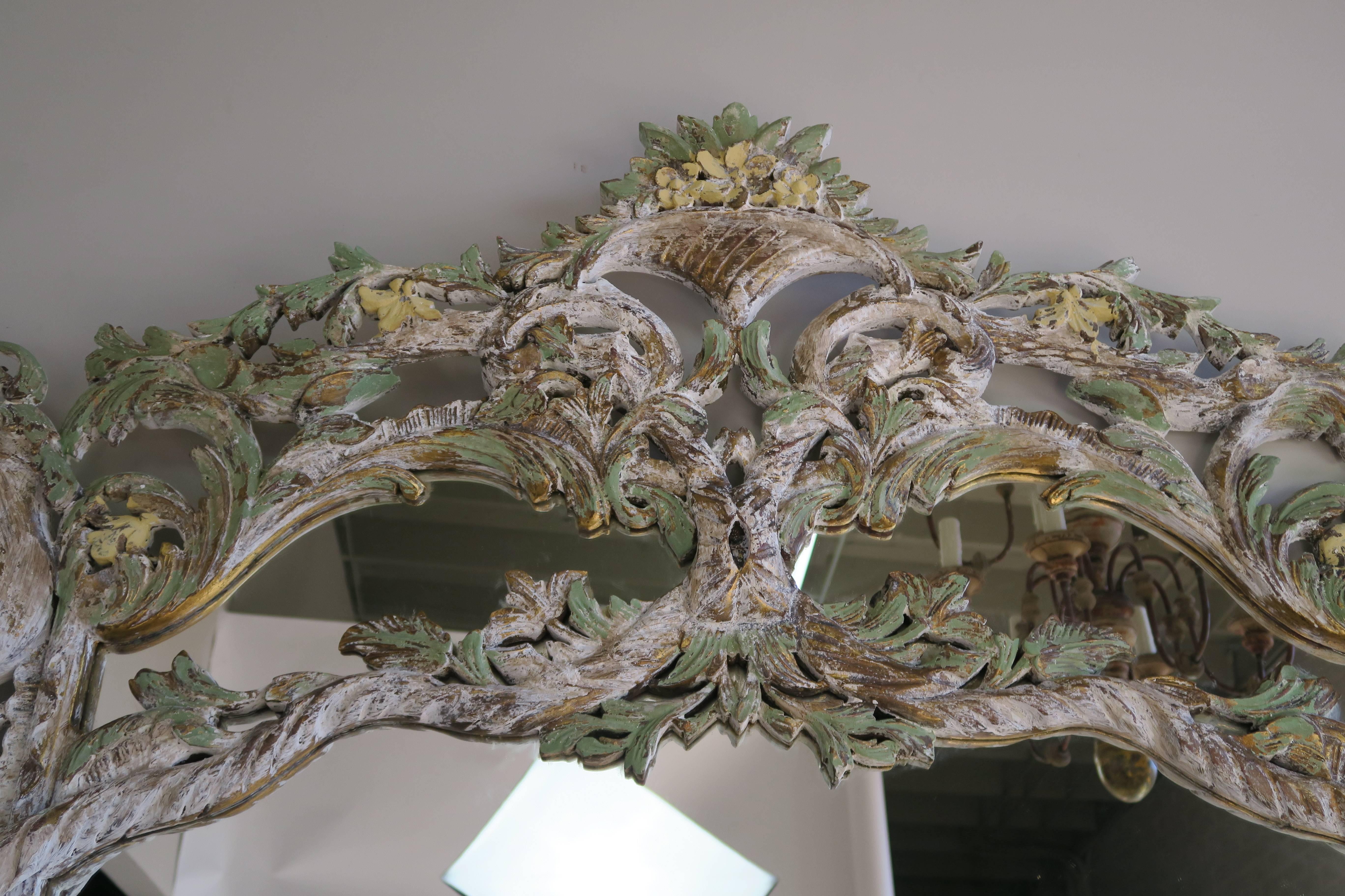 Monumental Italian Rococo style painted mirror with basket of flowers at top and cornucopias in both top corners. Carved garlands of flowers and swirling acanthus leaves throughout the detailed frame. Beautiful shades of antique white, green and