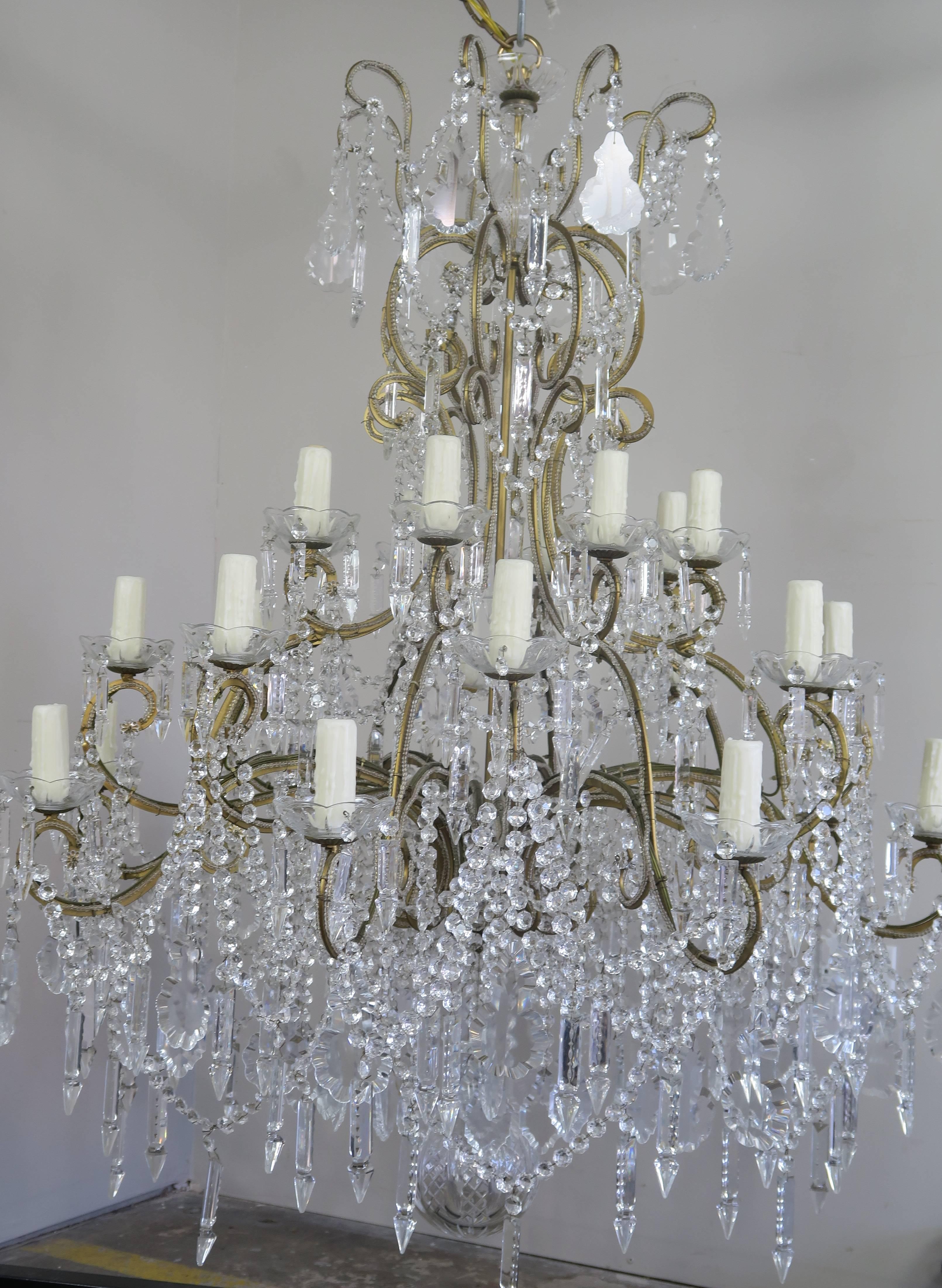 Monumental Italian 24 light crystal beaded arm chandelier adorned with garlands of crystal swags, crystal spheres, and crystal pendants throughout. The fixture is wired with new drip wax candle covers that sit on crystal bobeche. The cut crystal