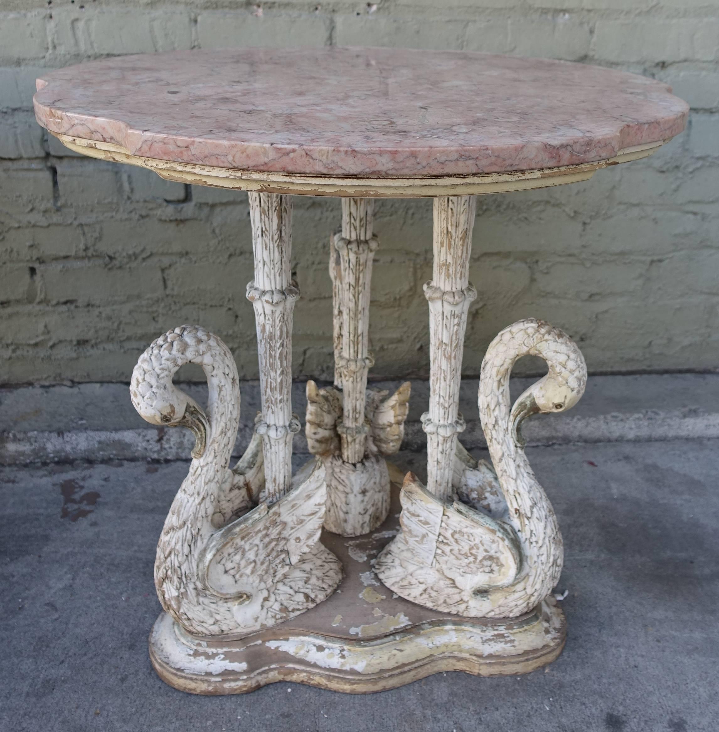 Pair of unique carved wood tables depicting a trio of swans. The tables have beautiful soft pink scalloped marble tops. Worn painted finish exposing the natural wood underneath.