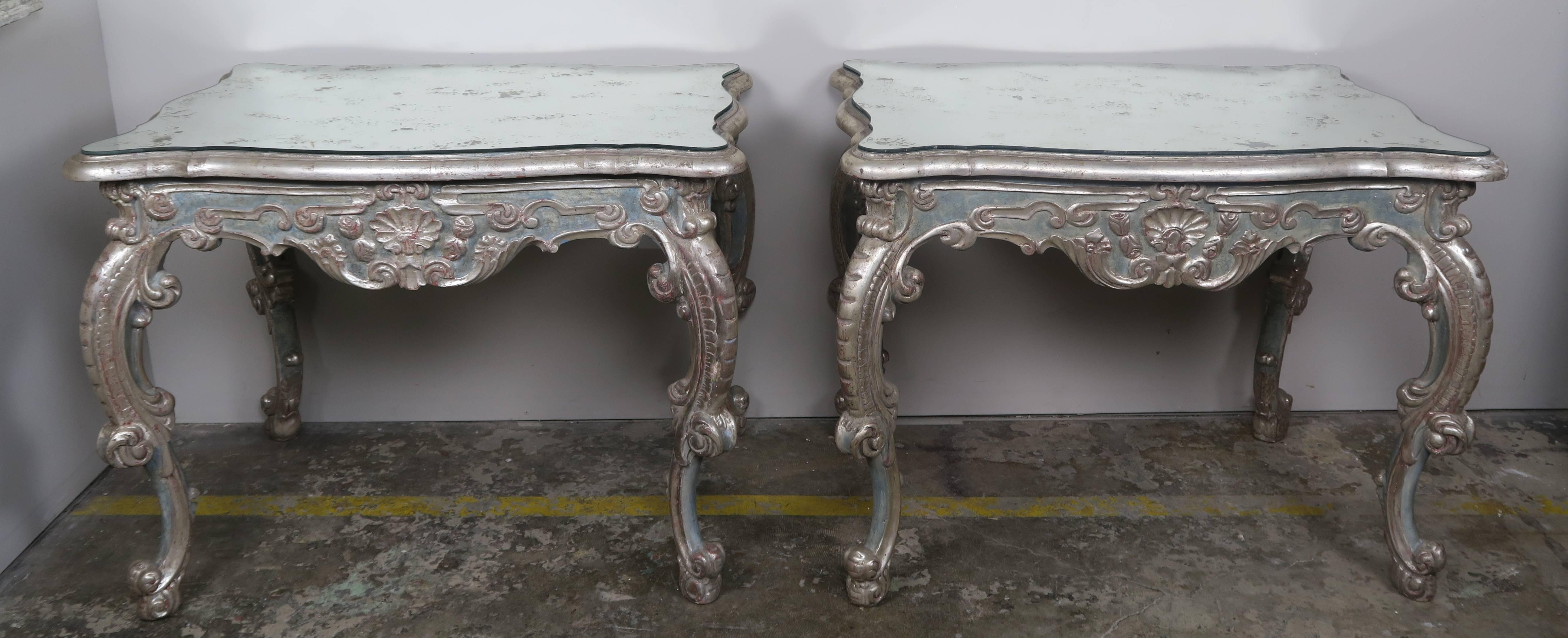 Pair of French painted and silver gilt carved wood tables standing on four cabriole legs with ram's head feet. Beautiful carving throughout. Antique mirrored serpentine shaped tops.