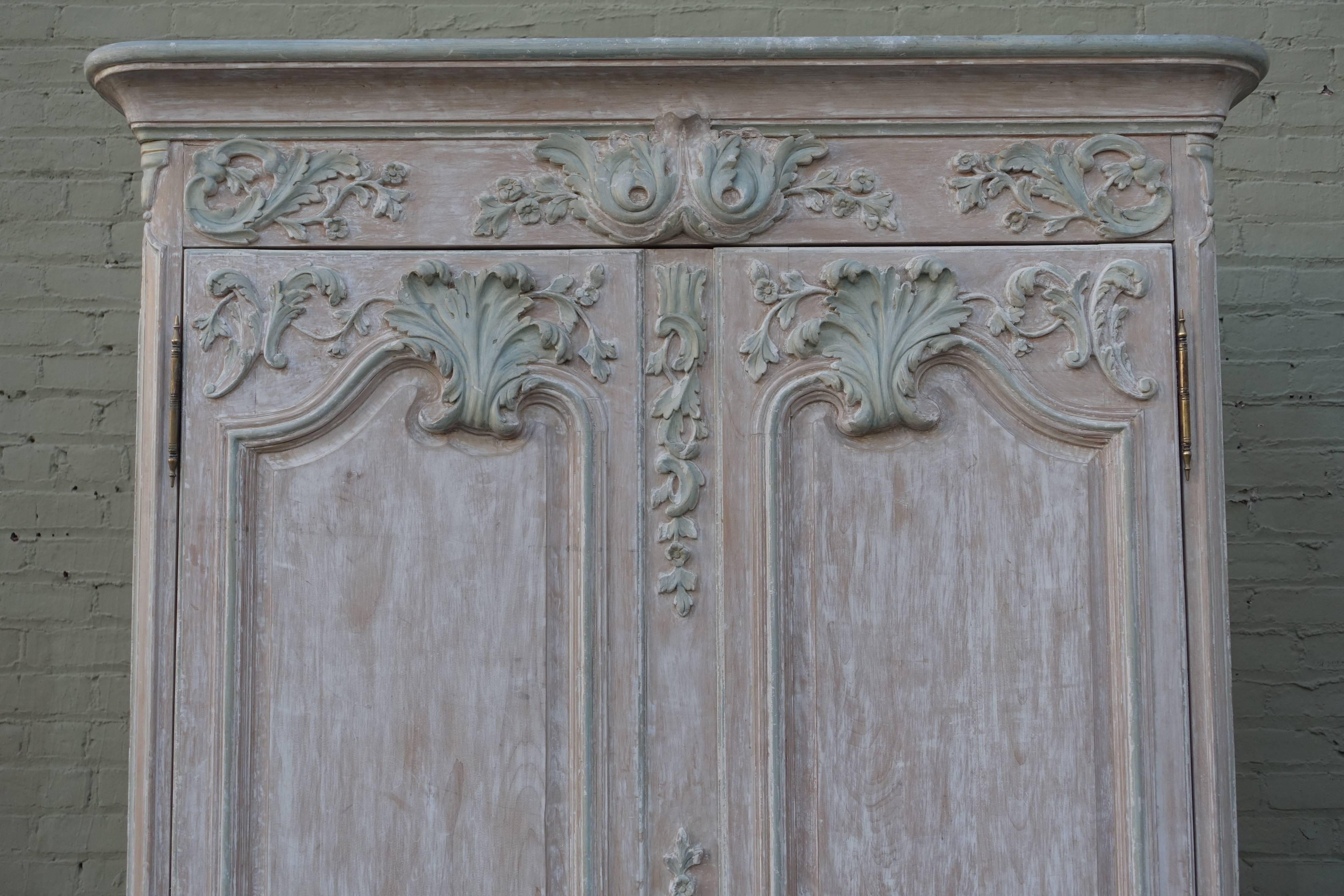 French Louis XV style carved painted armoire in soft colors of cream and seafoam green. The armoire stands on four cabriole legs with ram's head feet. Brass hardware.