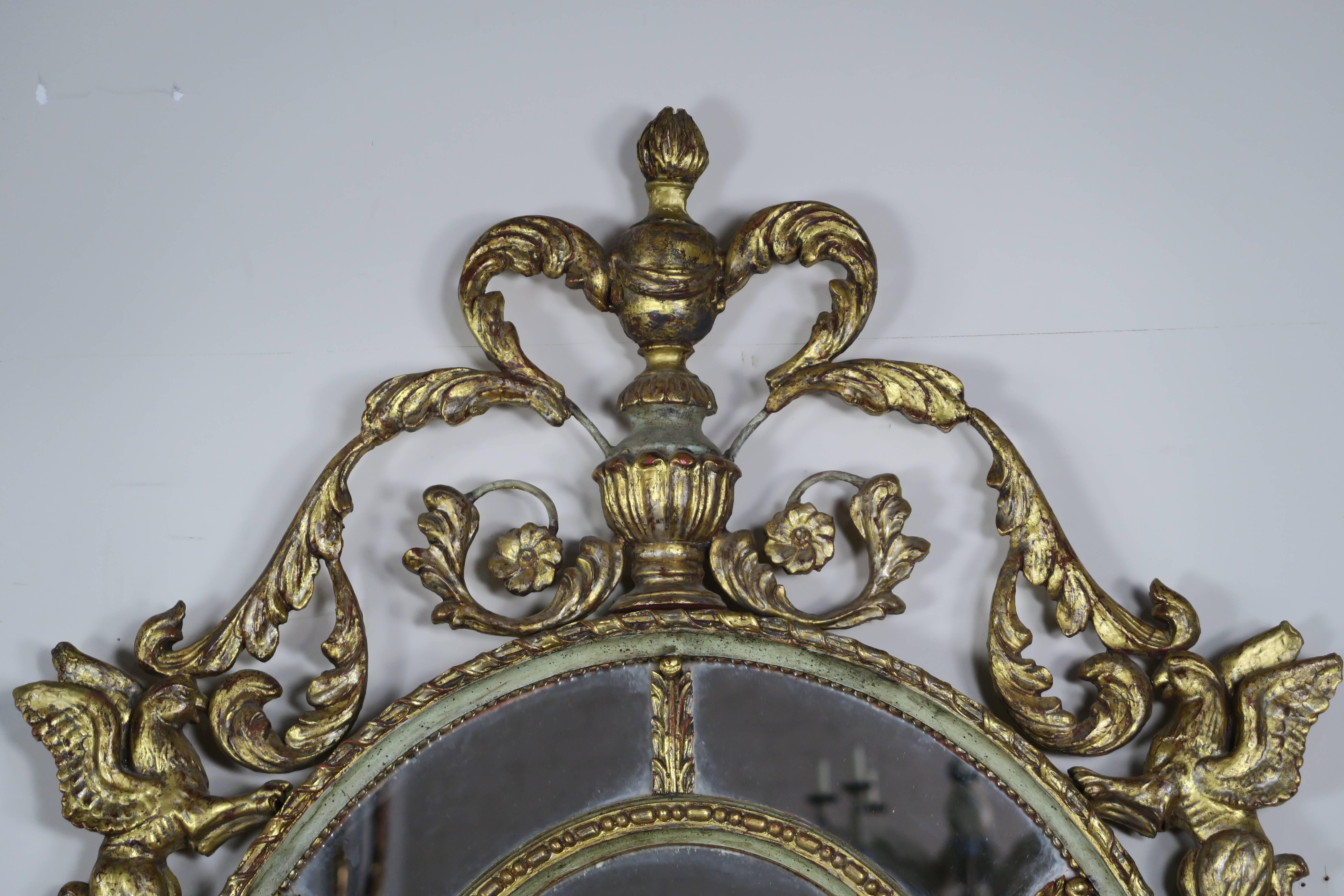 Pair of French Rococo style celadon painted and gold leaf mirrors in an oval shape with giltwood swirling acanthus leaves and flowers throughout. Griffins flank both sides of the mirrors.