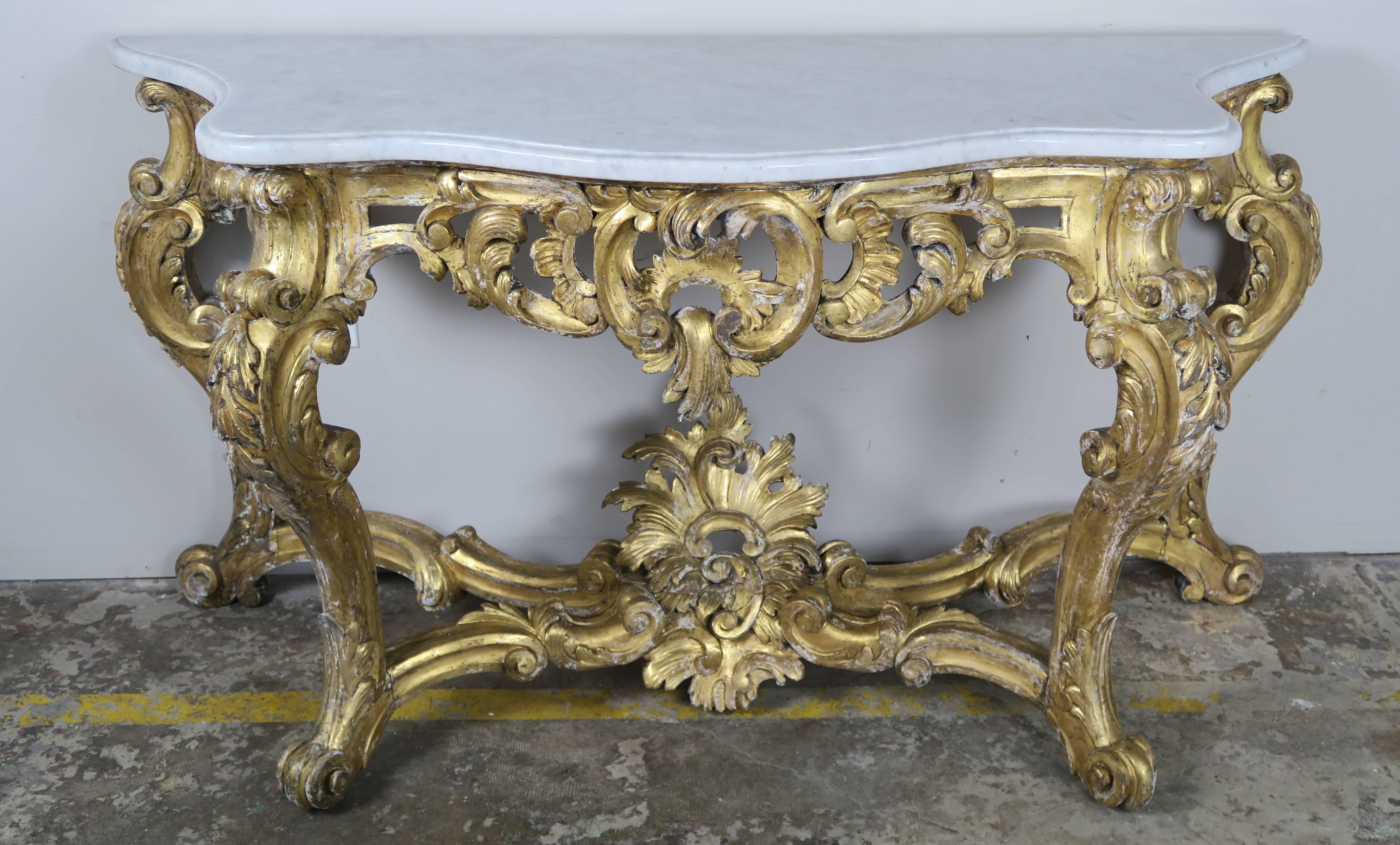 19th century French Louis XV Rococo style serpentine shaped giltwood carved console with original Carrara marble top. The console stands on four scrolled cabriole legs ending in ram's head feet. A bottom stretcher attaches the four legs to a centre