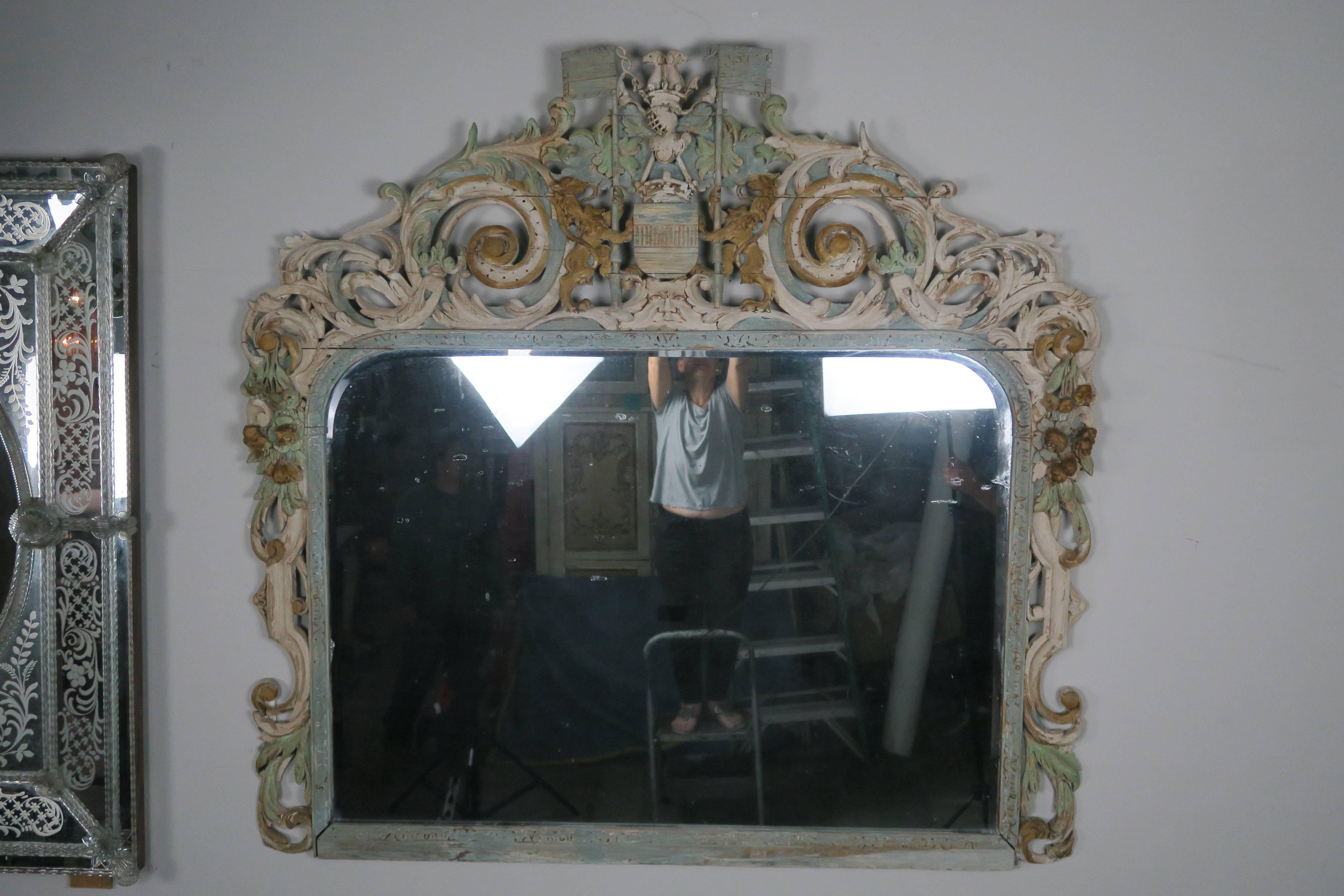 19th century English carved painted mirror with a pair of lions holding a coat of arms and surrounded by swirling acanthus leaves and carved flowers throughout.