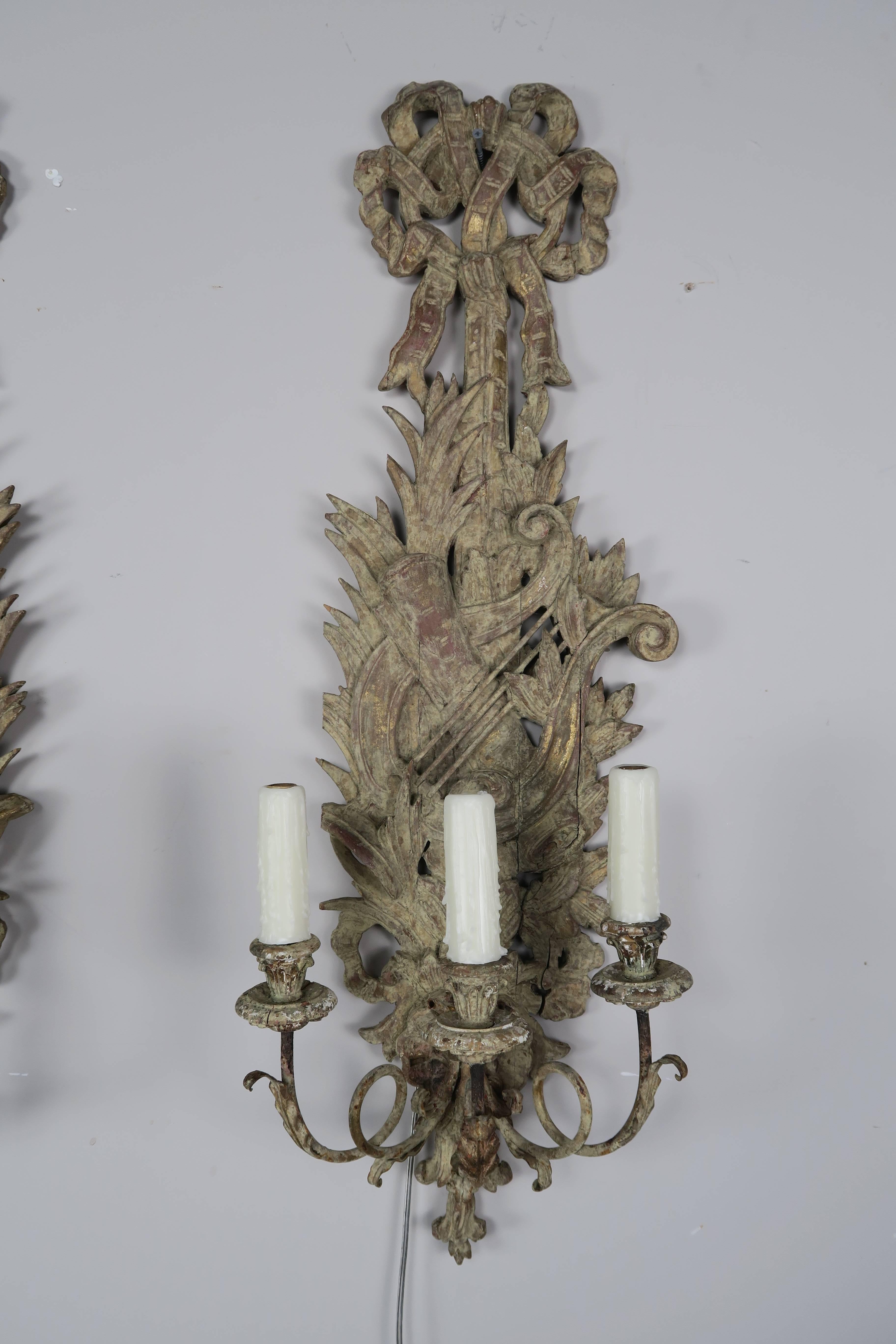Pair of French three-light carved wood sconces with musical instruments, ribbon and laurel leaves throughout. Remnants of gold leaf throughout. Newly rewired with drip wax candle covers.