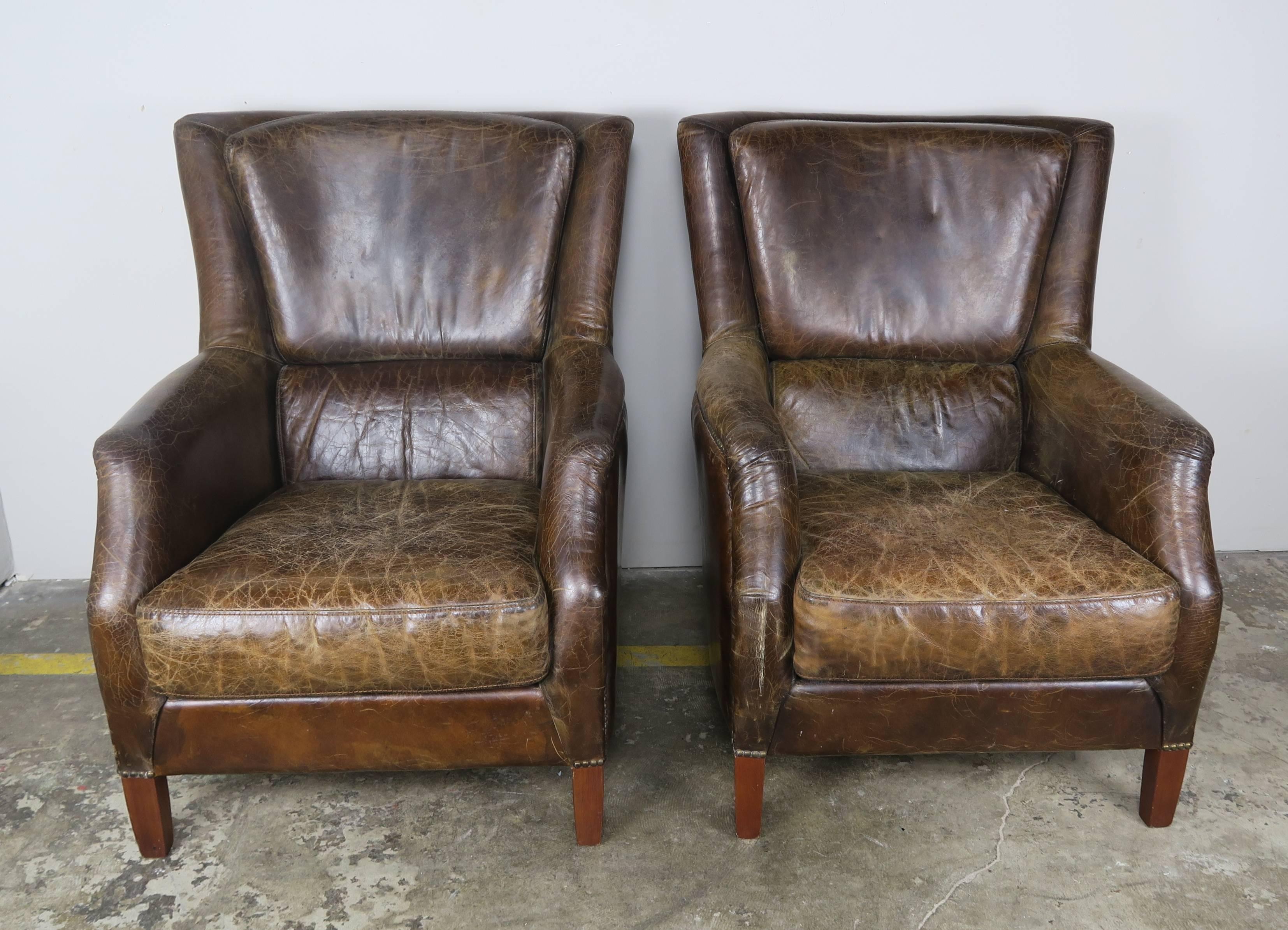 Pair of French deco style tobacco colored leather upholstered armchairs with loose seat cushions and nailhead trim detail. The armchairs stand on four walnut straight tapered legs.