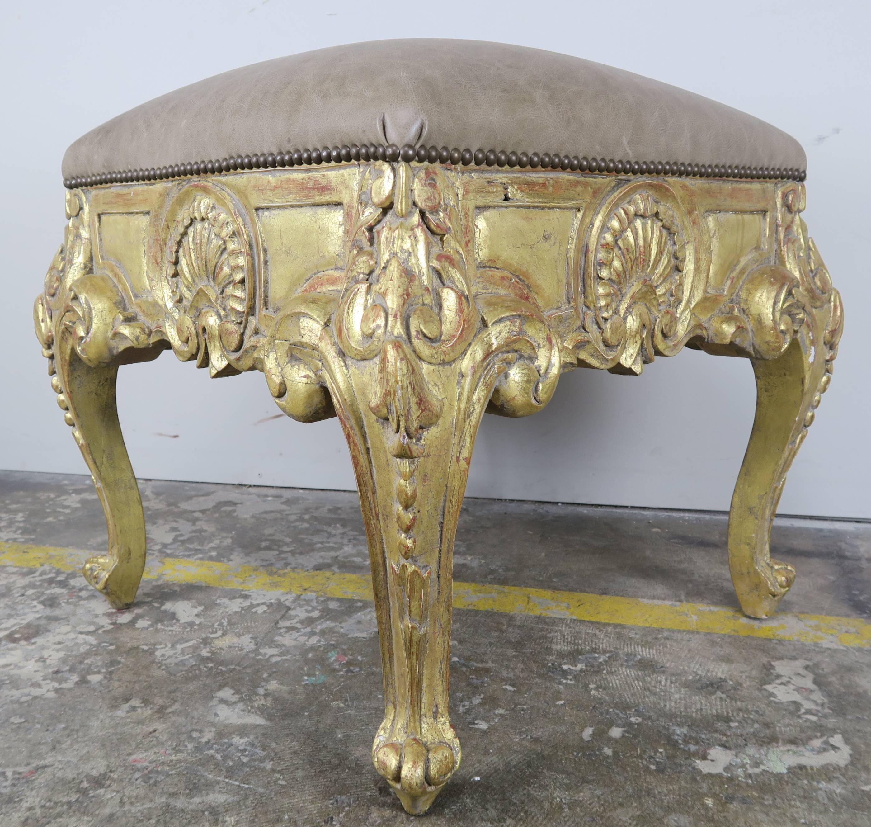 Pair of French Louis XV style giltwood benches standing on four cabriole legs and ram's head feet. Carved shells and acanthus leaves throughout. Upholstered in an elegant taupe leather with nailhead trim detail.