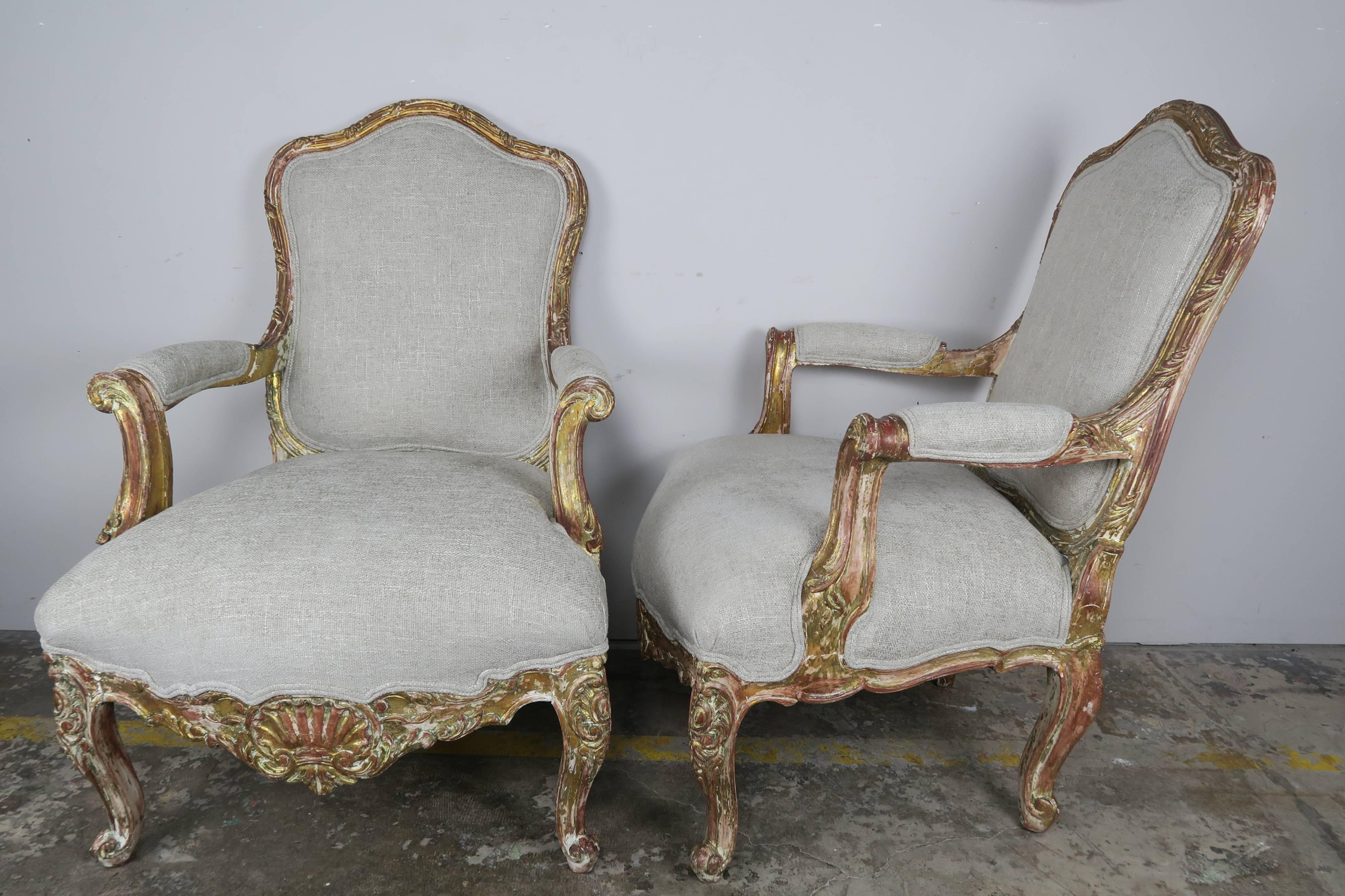 Pair of French carved giltwood Louis XV style armchairs standing on four cabriole legs with beautiful carved shell detail and rolled arms. Newly upholstered in a heavy textured linen with double self cord detail.