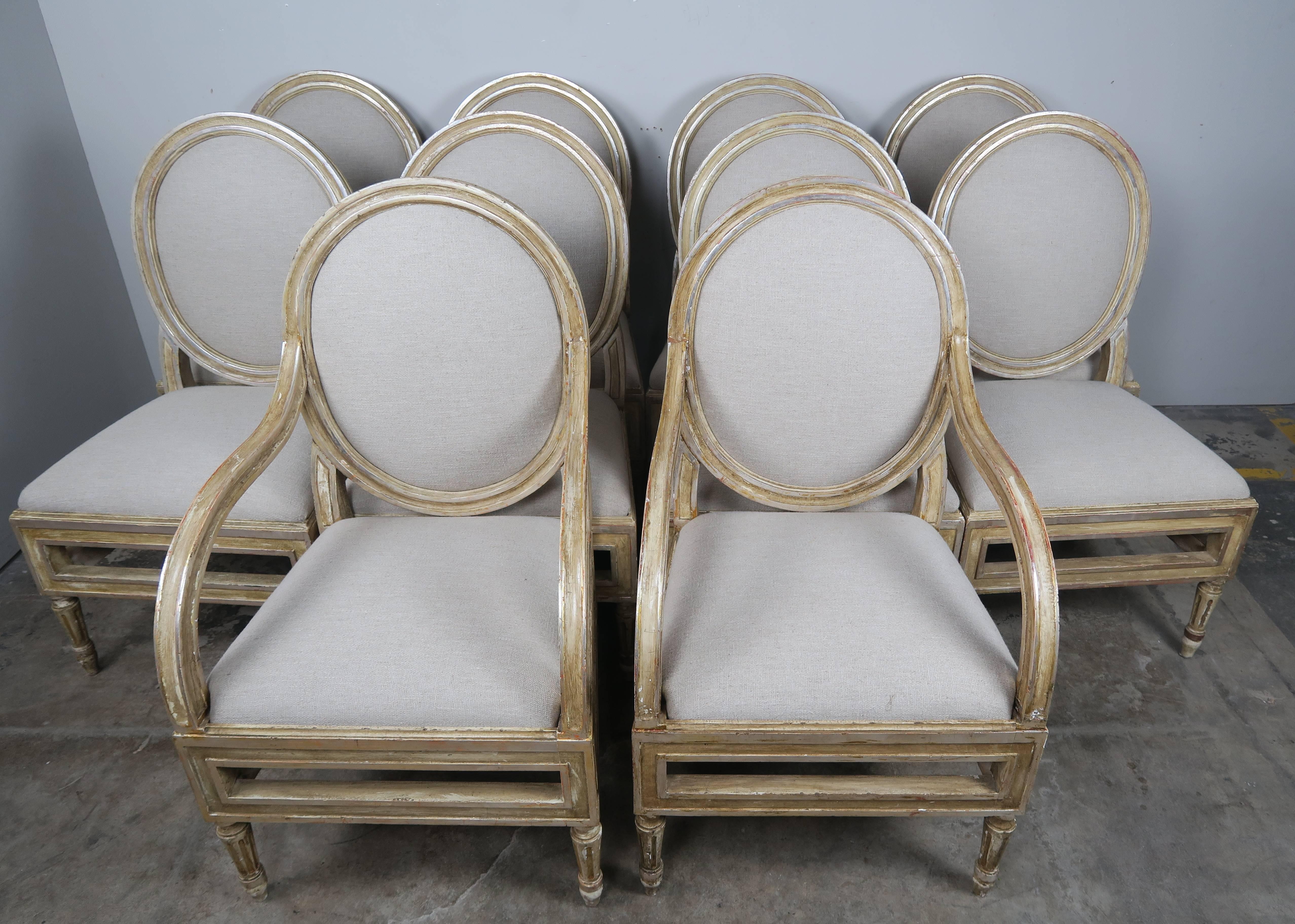 Set of ten Italian Louis XVI style painted and parcel silver gilt dining chairs standing on straight fluted legs with oval backs. The chairs have been newly upholstered in a Belgium linen.