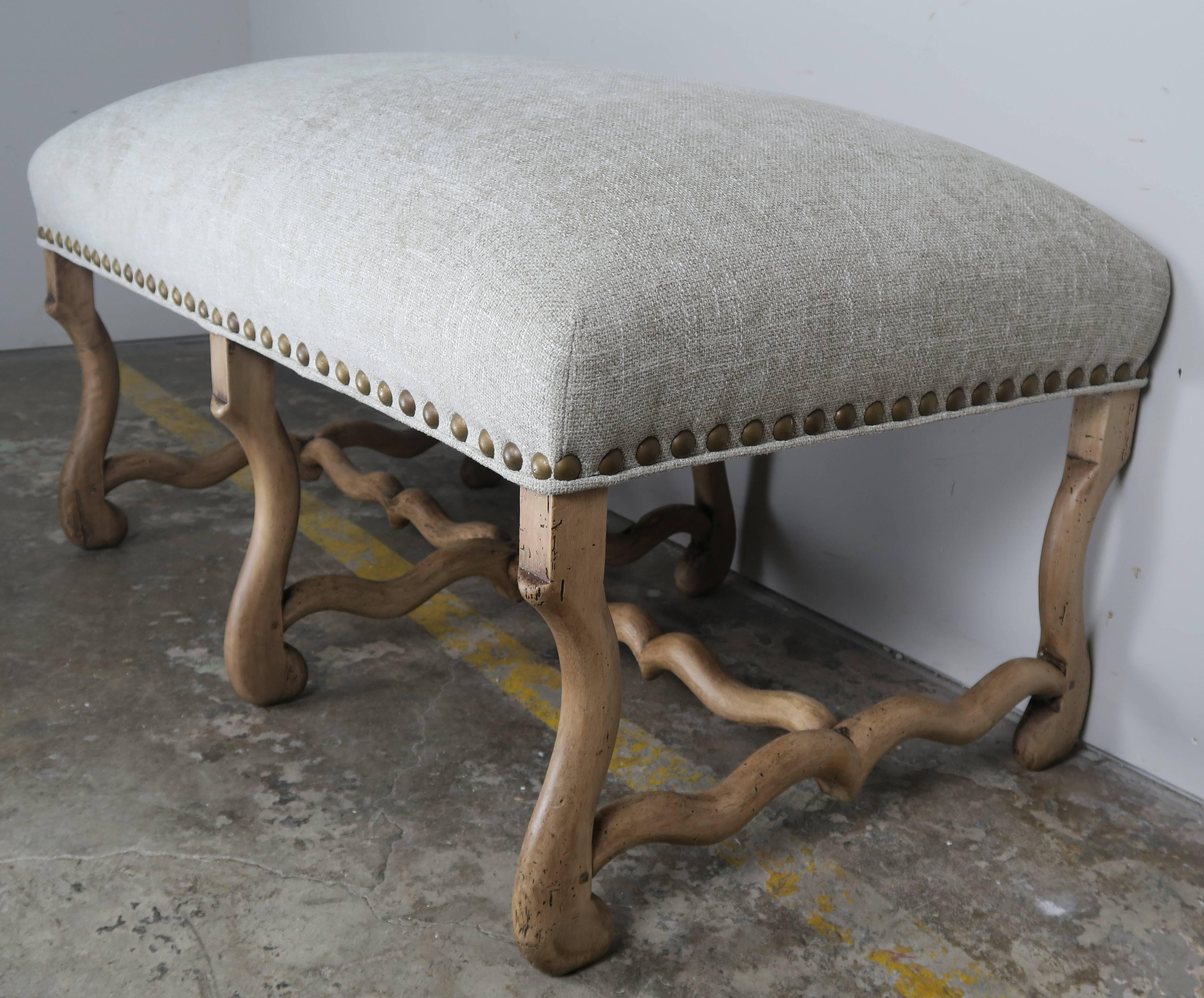 Spanish walnut bench with simple graceful lines connecting six legs to centre stretchers. Newly upholstered in Belgium linen with large brass nailhead trim detail.