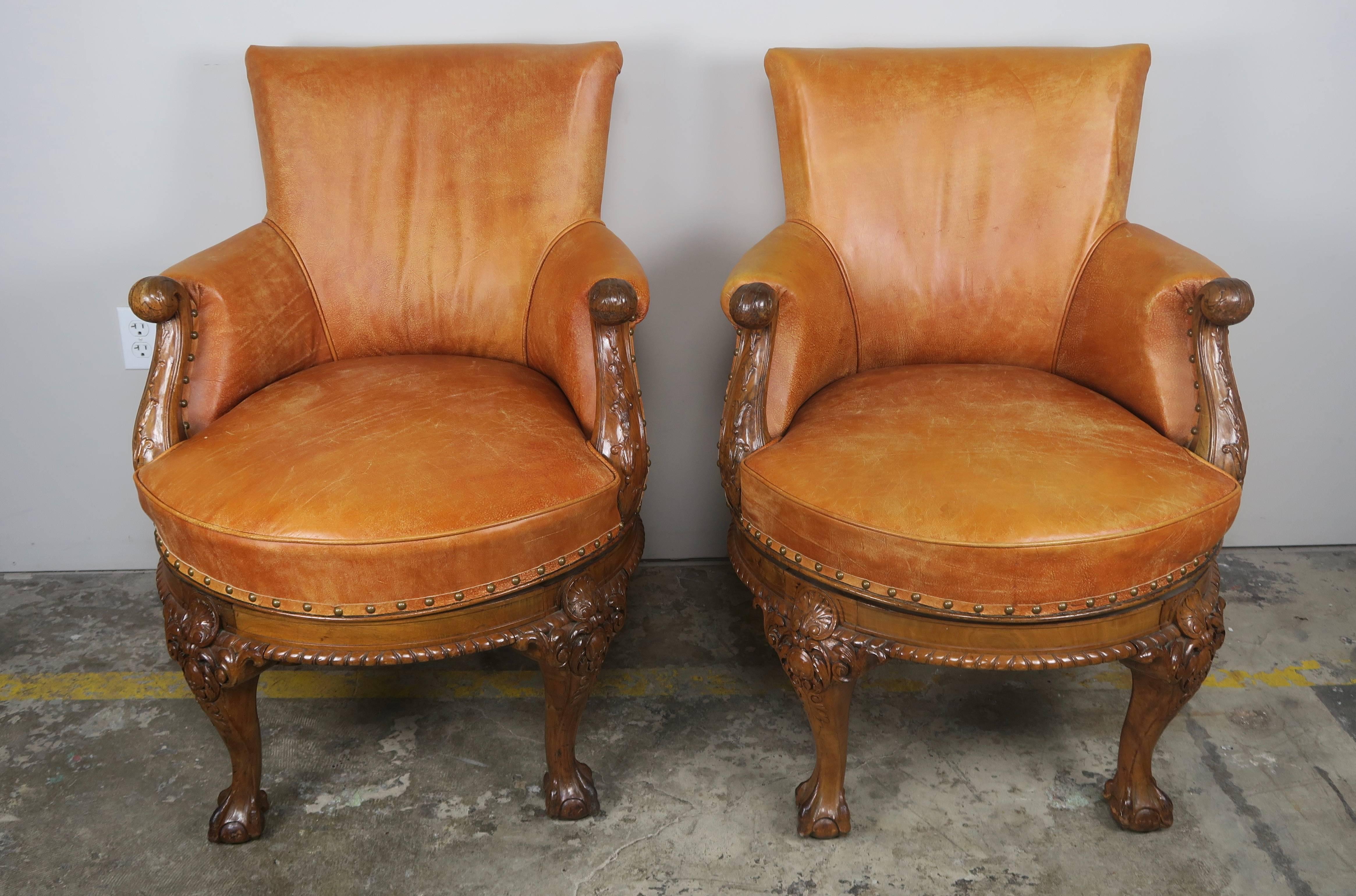 Pair of English George II style walnut swivel library chairs upholstered in original caramel colored leather with leather gimp and spaced nail head trim detail. The chairs stand on four beautifully carved legs ending in ball and claw feet.
