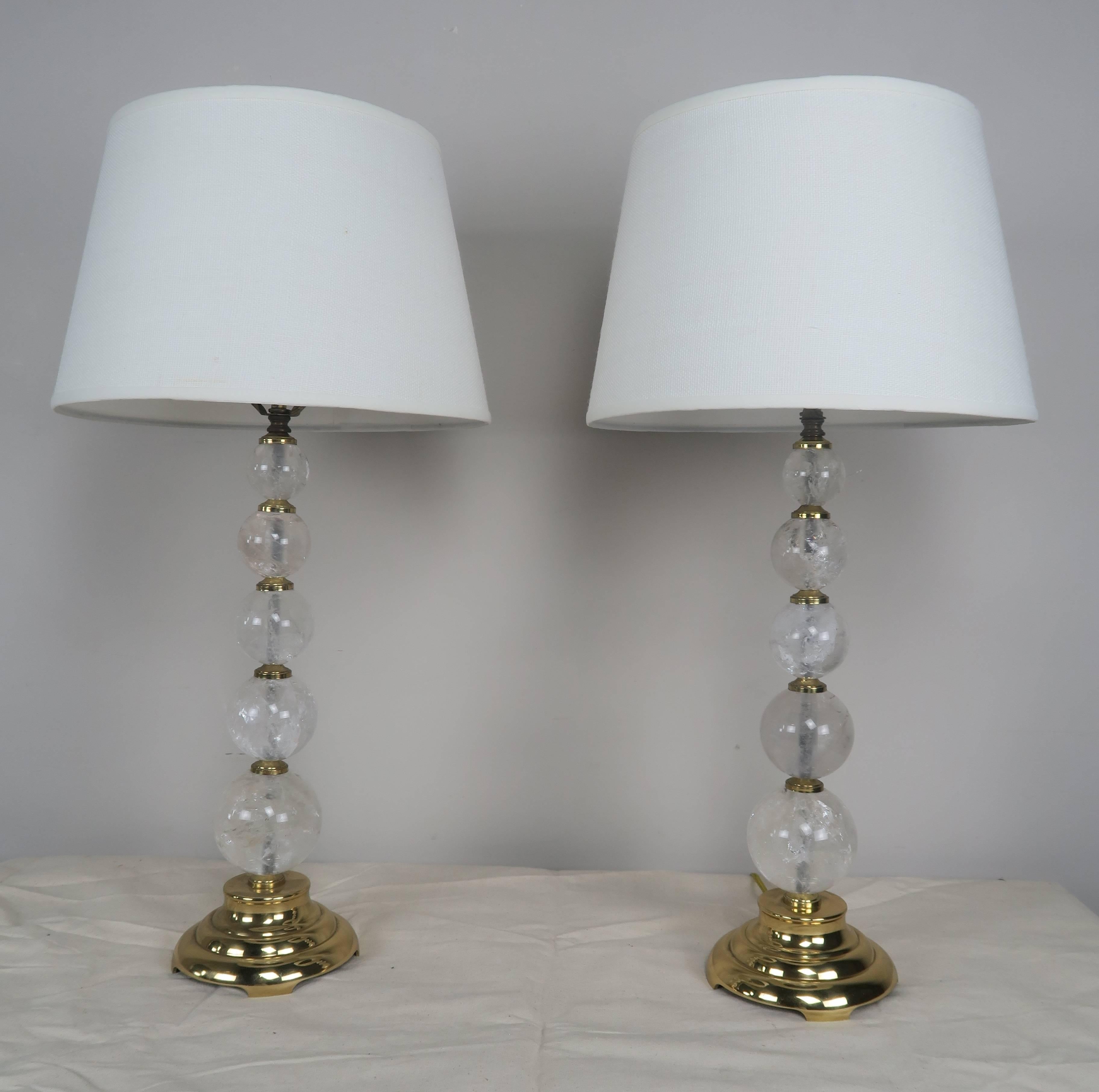 Five-rock crystal spheres make up the stem of these table lamp with polished brass bases. Rock crystal is antique from Brazil, but carved in the US. The lamps are crowned with custom white linen shades. The lamps are newly rewired and are ready to