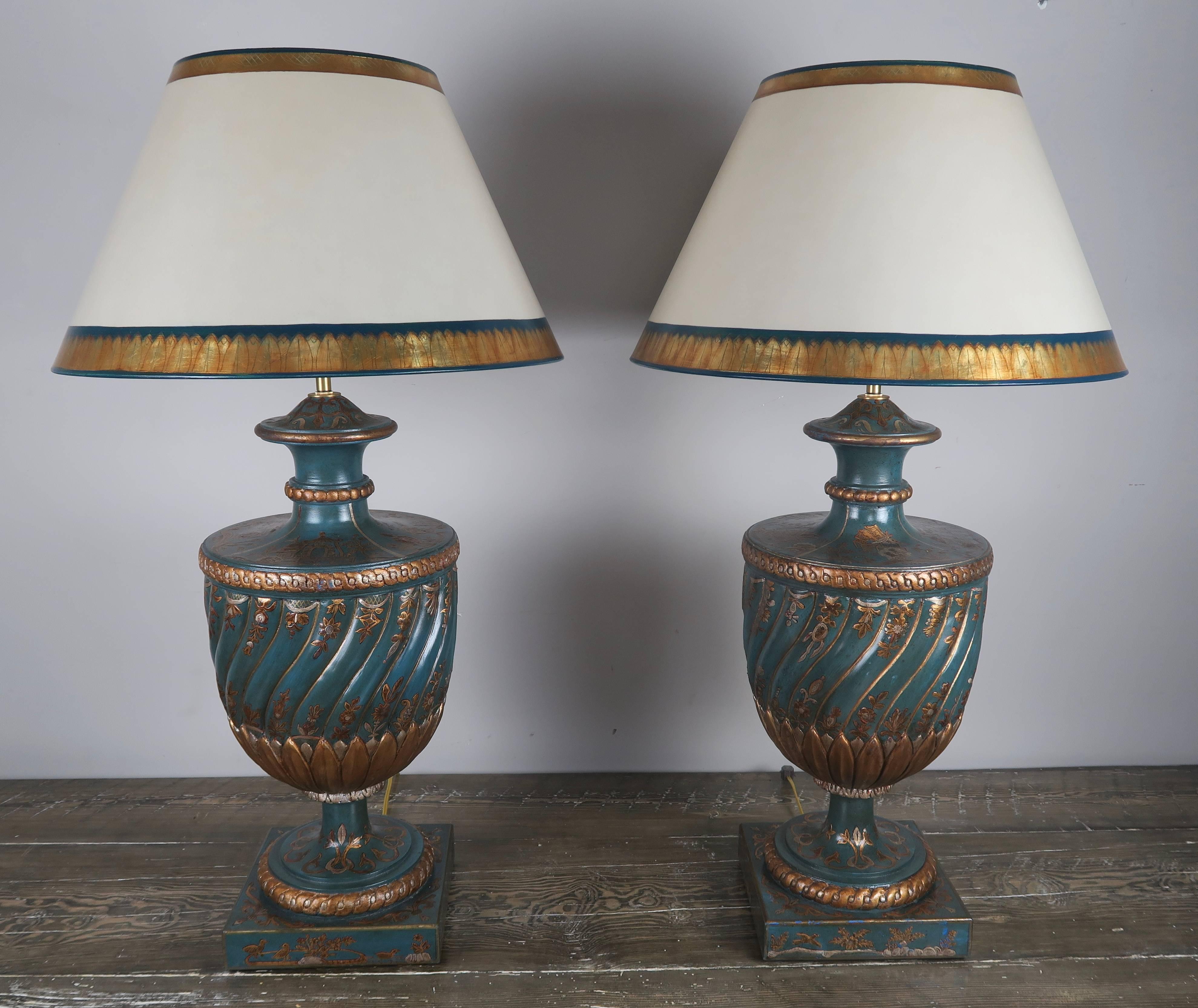 Pair of teal and raised gold chinoiserie decorated urn lamps that have been crowned with hand-painted parchment shades. The lamps are newly wired and are in working condition with two standard sockets each lamp. 


Shade size: 10