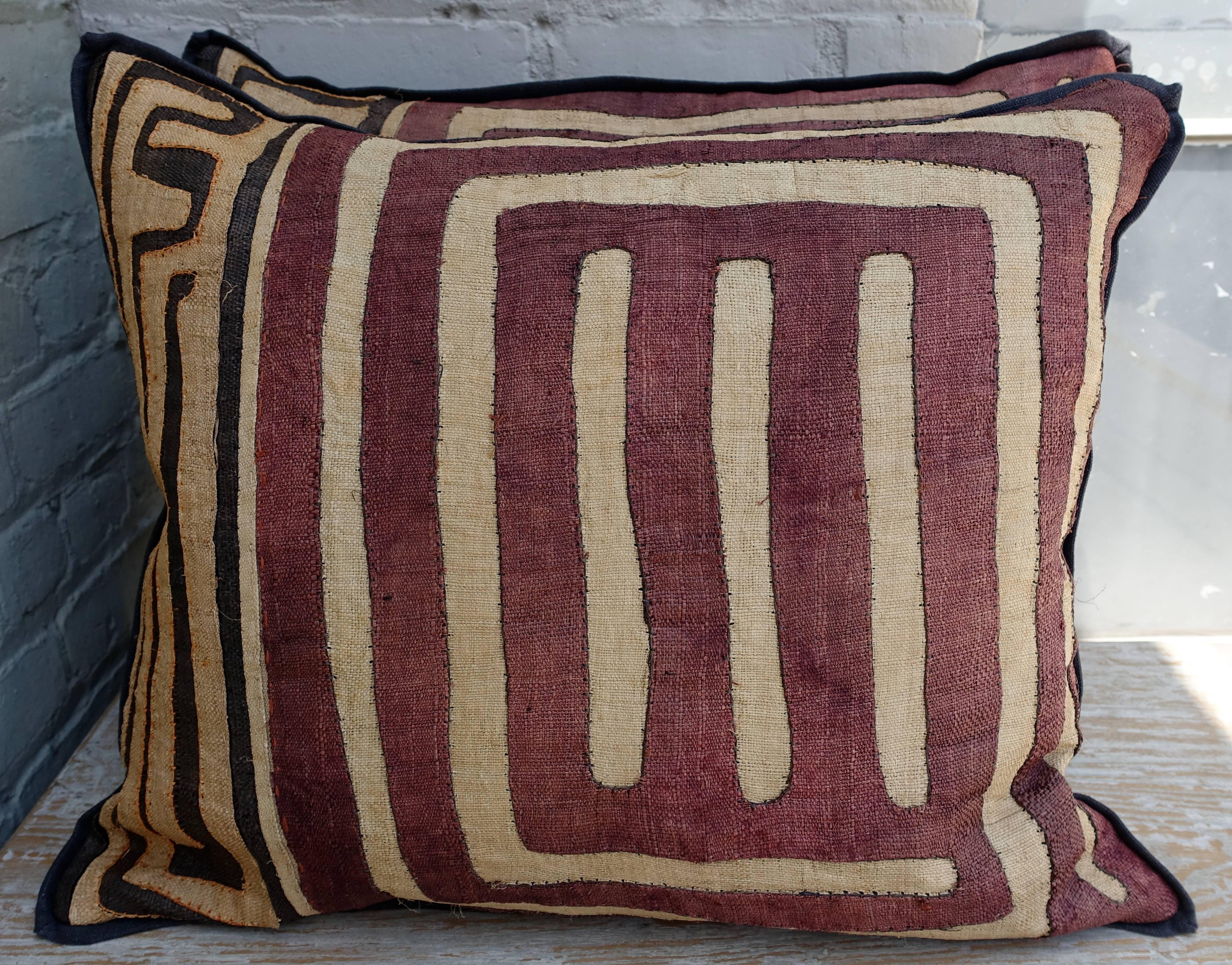 A pair of large rectangular custom designed African Kuba cloth pillows. Aubergine and black raffia fronts. Black linen backs with self welt detail. Down inserts, sewn closed.