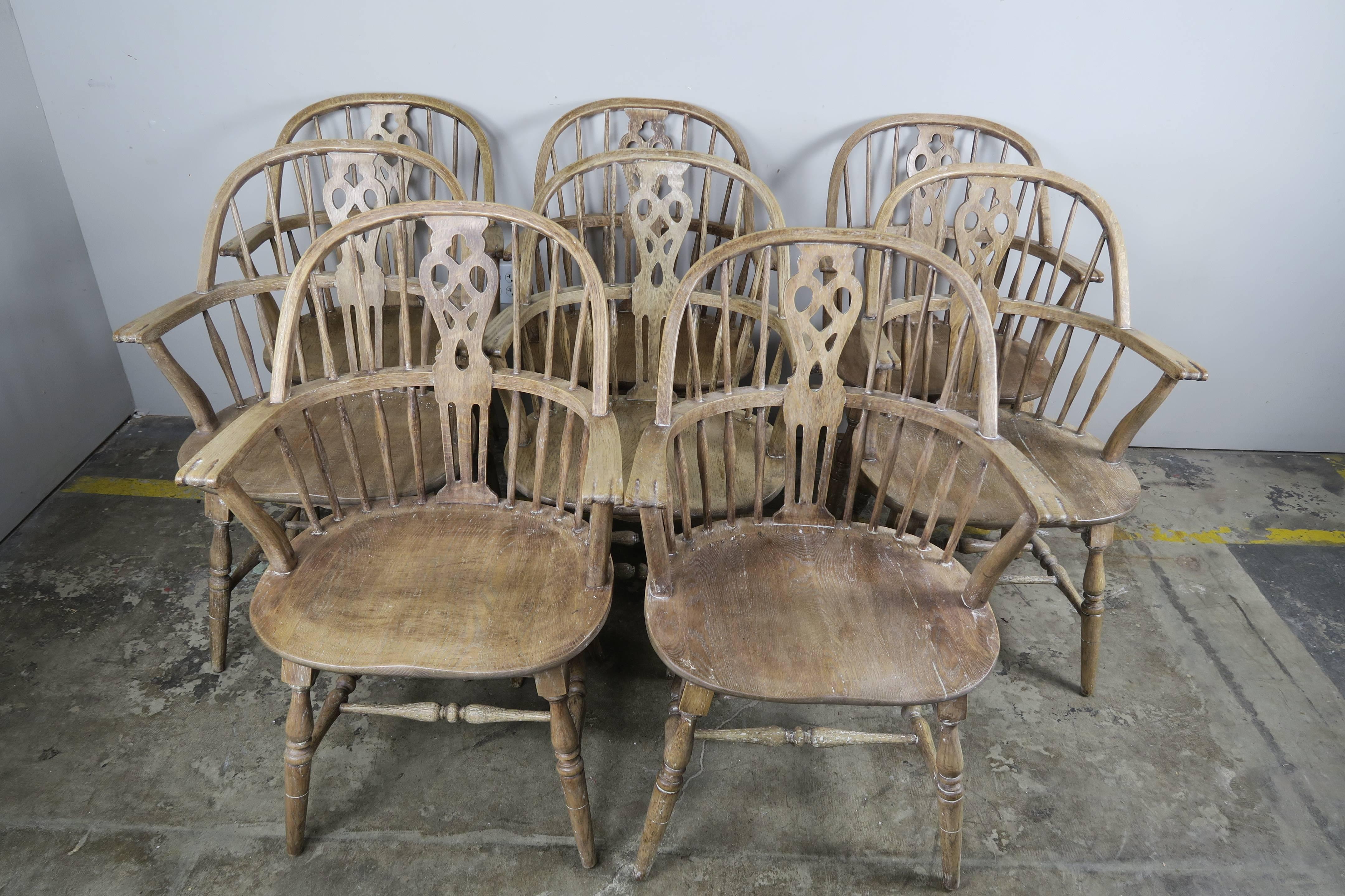 Set of handcrafted eight elmwood windsor style armchairs in a slightly white washed finish with spindle and pierced splat backs, scrolled arms, saddle seats, and turned legs with connecting stretchers.