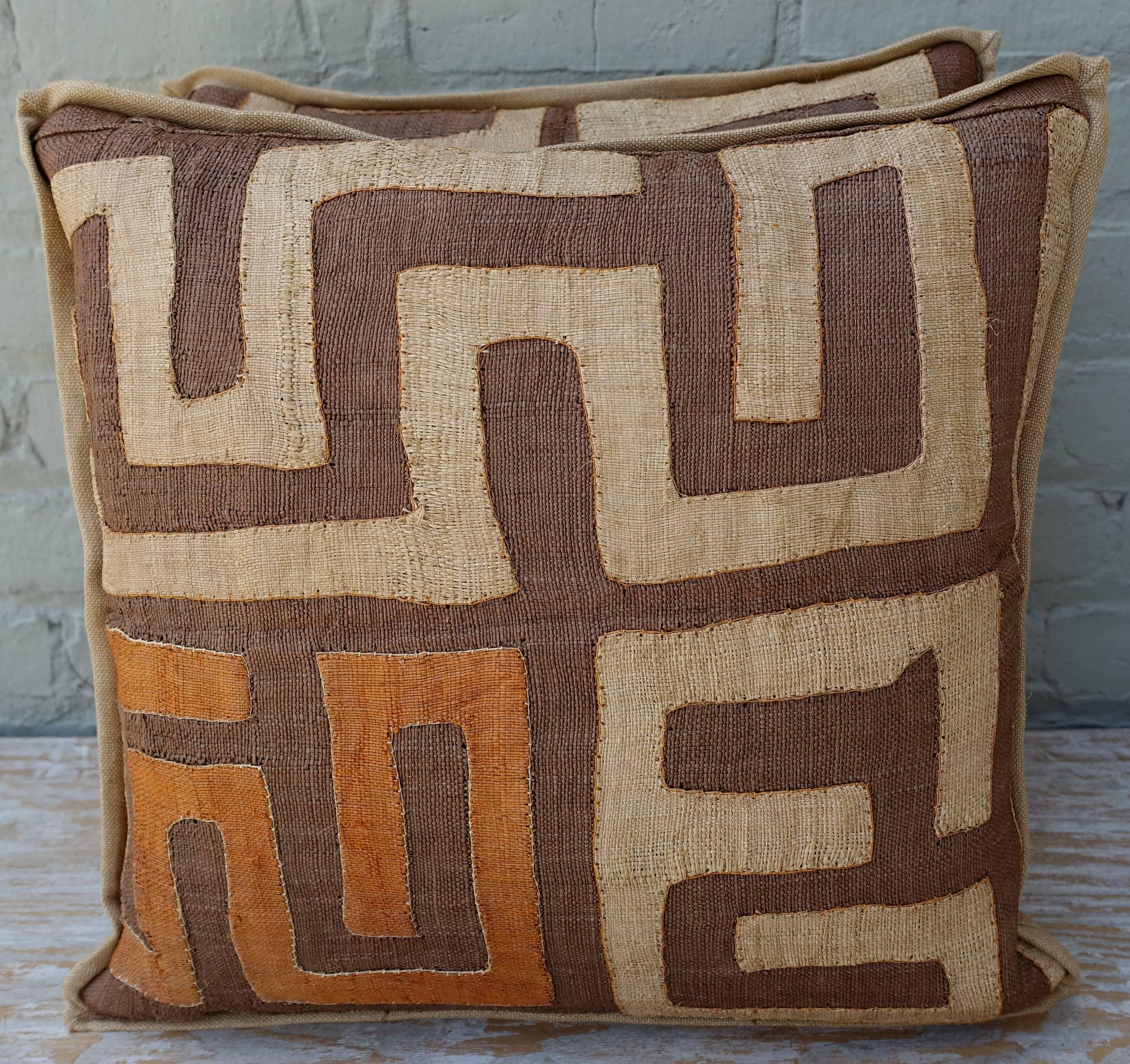 Pair of square shaped brown, wheat and brick orange colored Kuba cloth pillows made with natural raffia African Kuba cloth fronts and natural colored linen backs and self 1/2