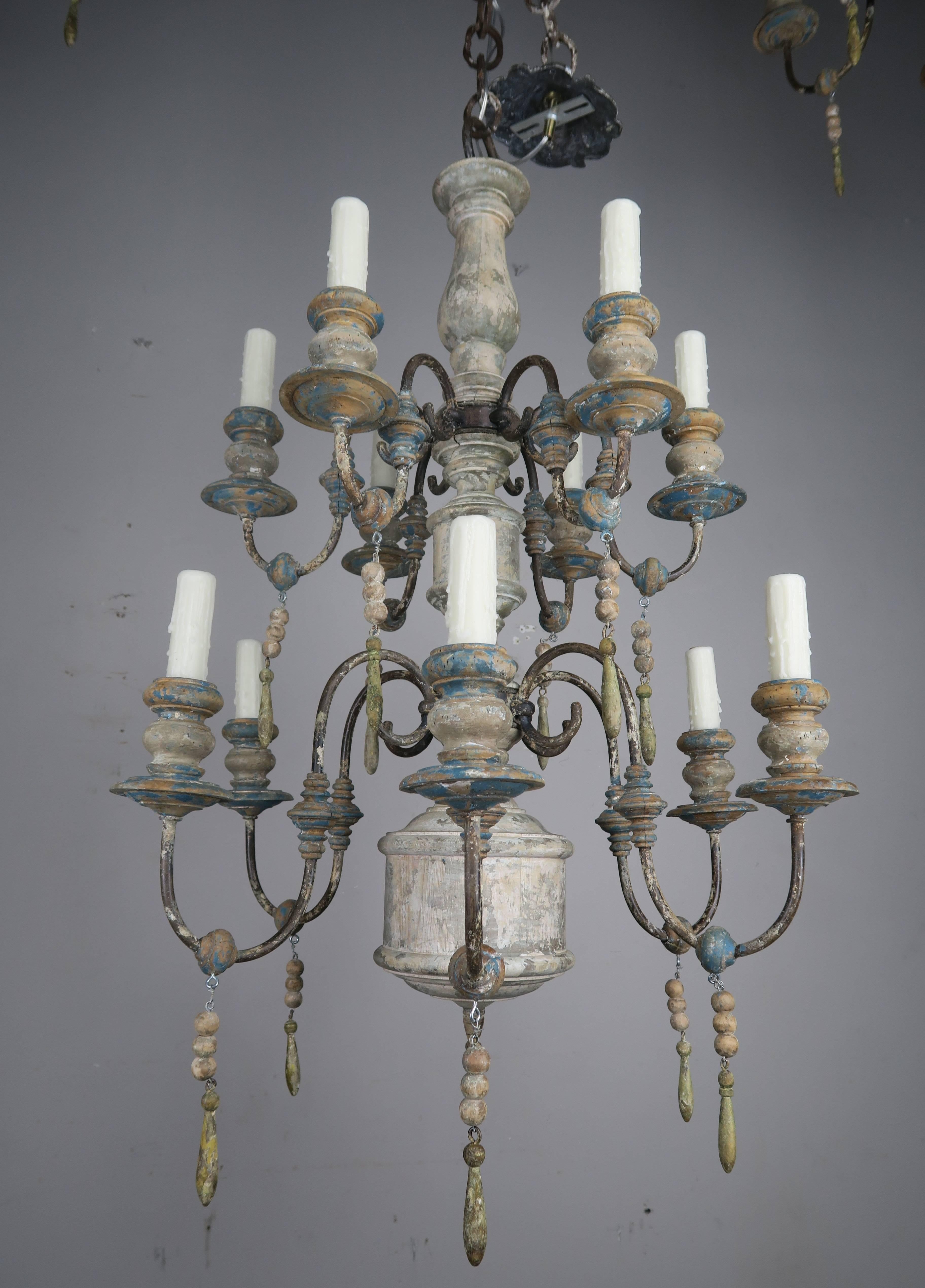 Pair of twelve-light wood and iron painted chandeliers with wood drops throughout. The chandeliers have been newly rewired with drip wax candle covers. Chain and canopies included.