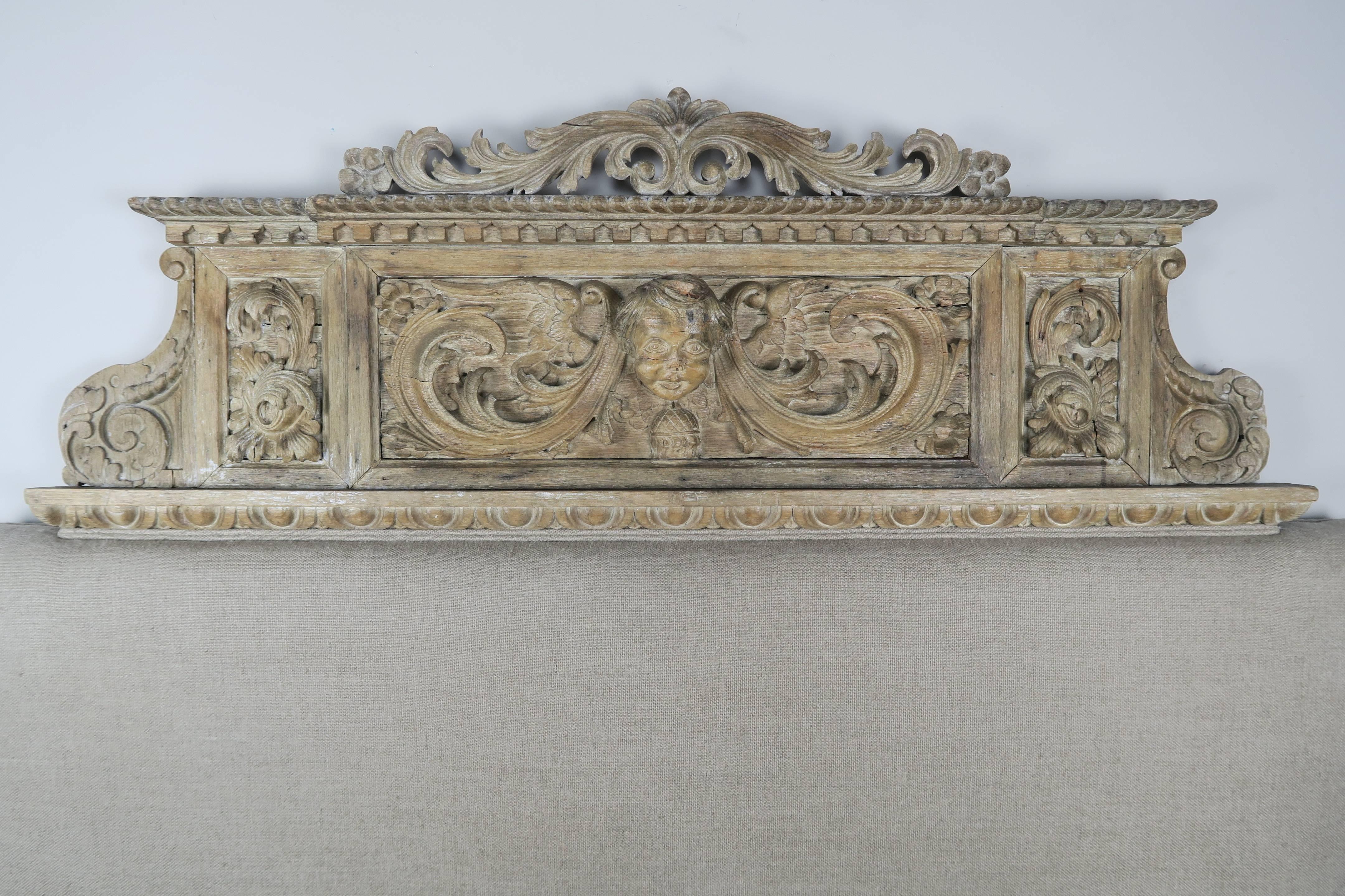 Queen-size washed Belgium linen headboard made with a 19th century carved wood panel depicting a cherub face surrounded by swirling acanthus leaves throughout. Egg and dart carved detail across the bottom of the panel. Additional carved details
