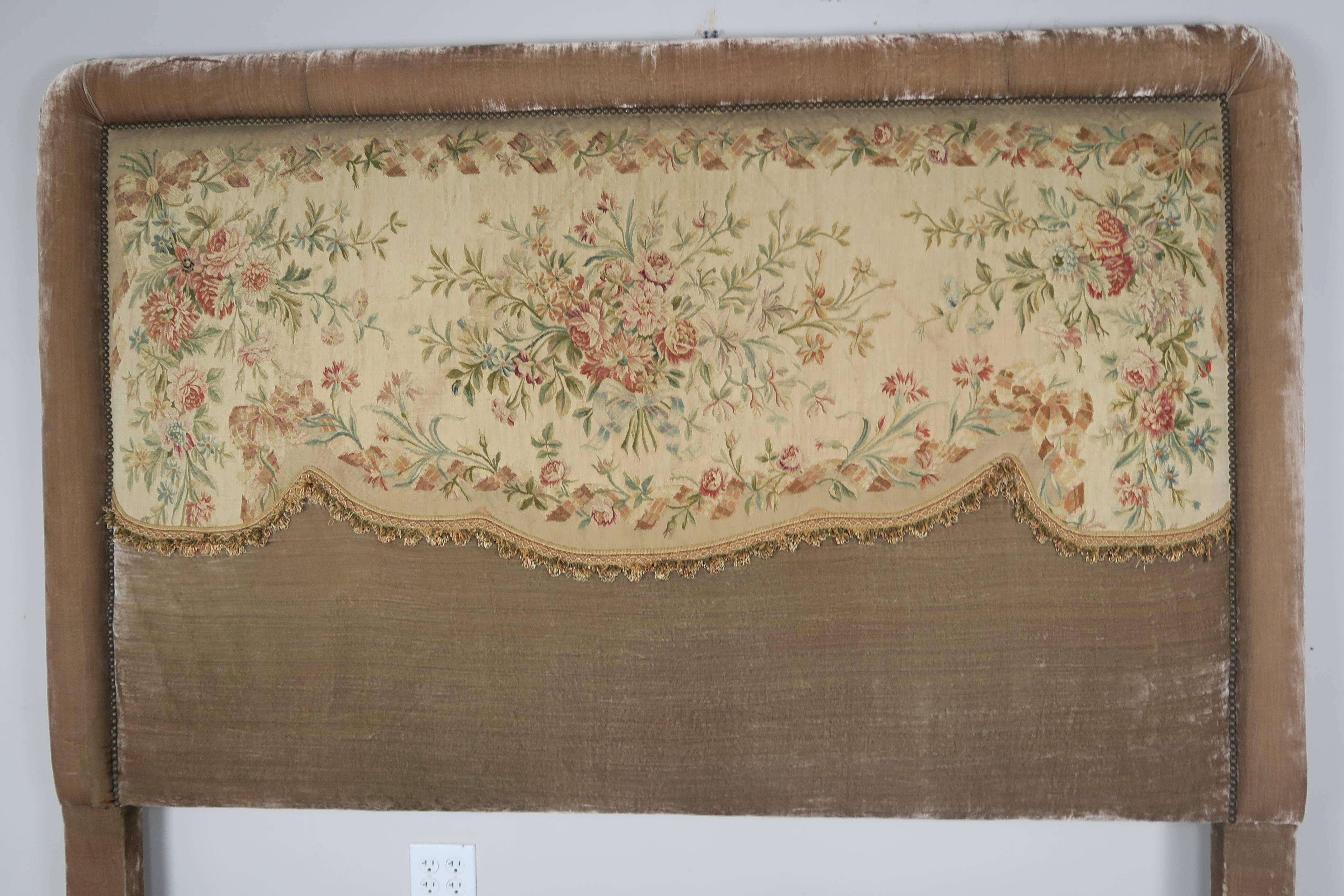 The rectangular headboard applied with a floral 19th century. Aubusson tapestry in a silk fringe, all enclosed in a bolstered muted rose colored velvet frame that is detailed with nail heads.