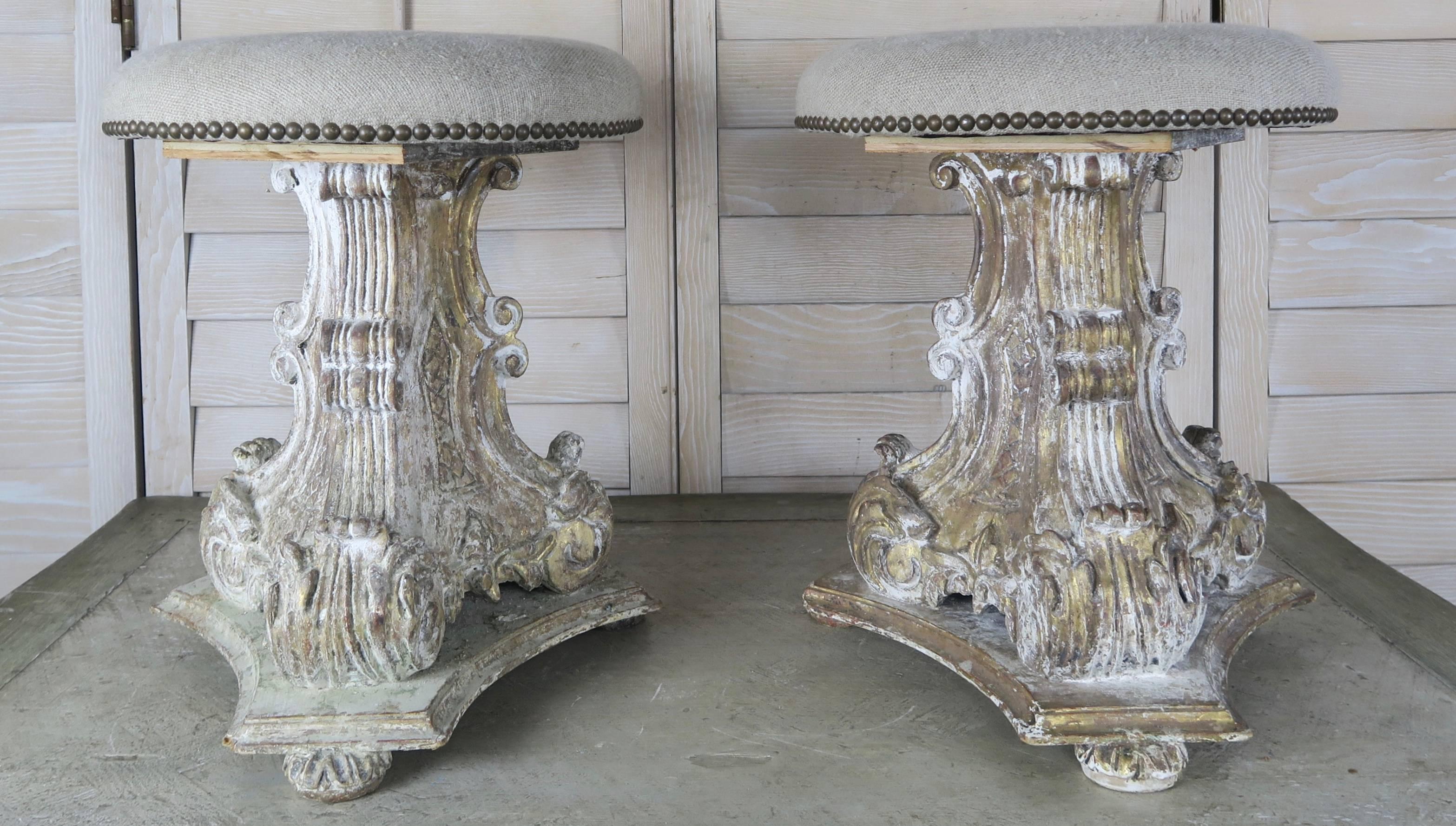 Pair of Italian carved wood painted and parcel-gilt stools newly upholstered in an oatmeal colored Belgium linen with brass nailhead trim detail. Remnants of gold leaf and gesso throughout.