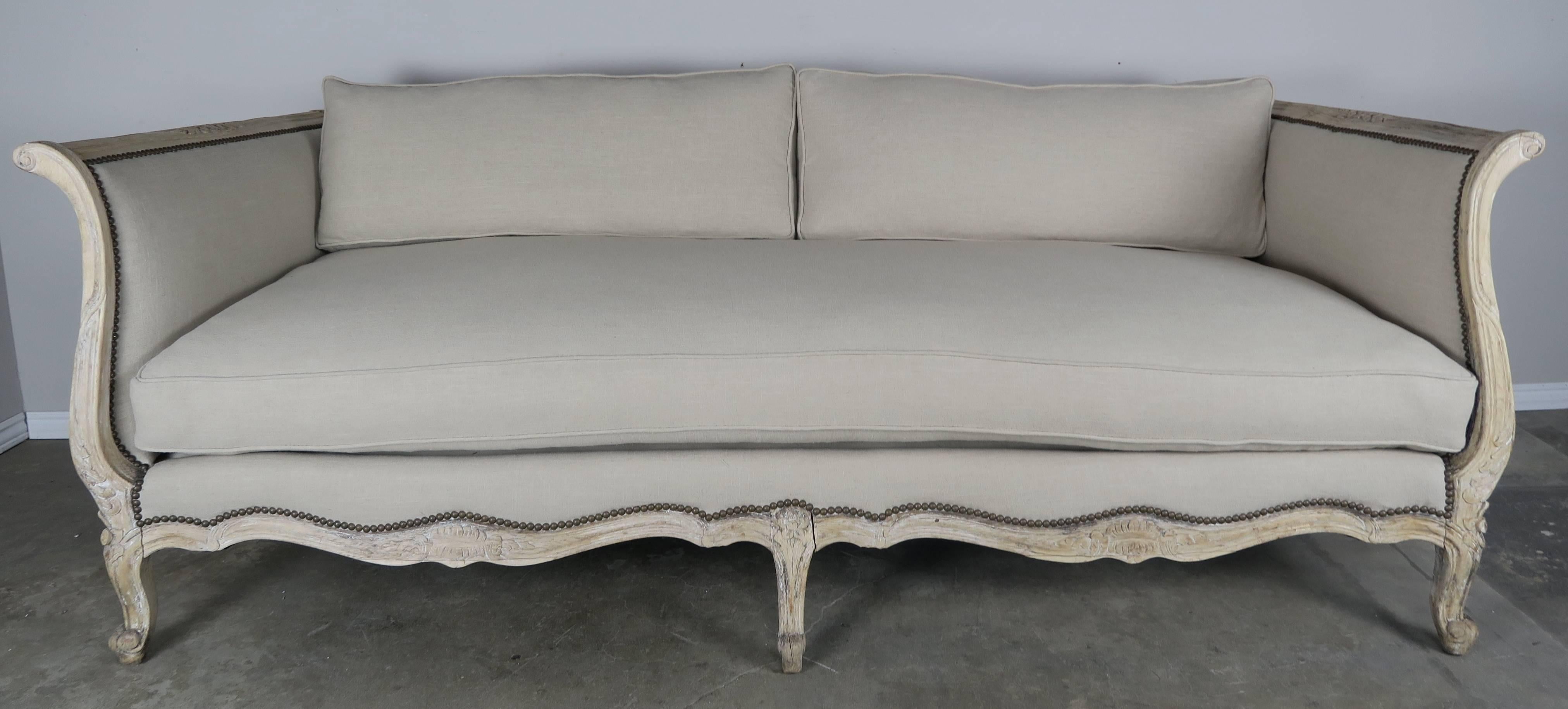 19th century French carved natural wood sofa newly upholstered in a natural colored linen and finished with antique brass colored nailheads. The Louis XV style sofa stands on six cabriole legs that end in ram's head feet. Loose down filled cushions.