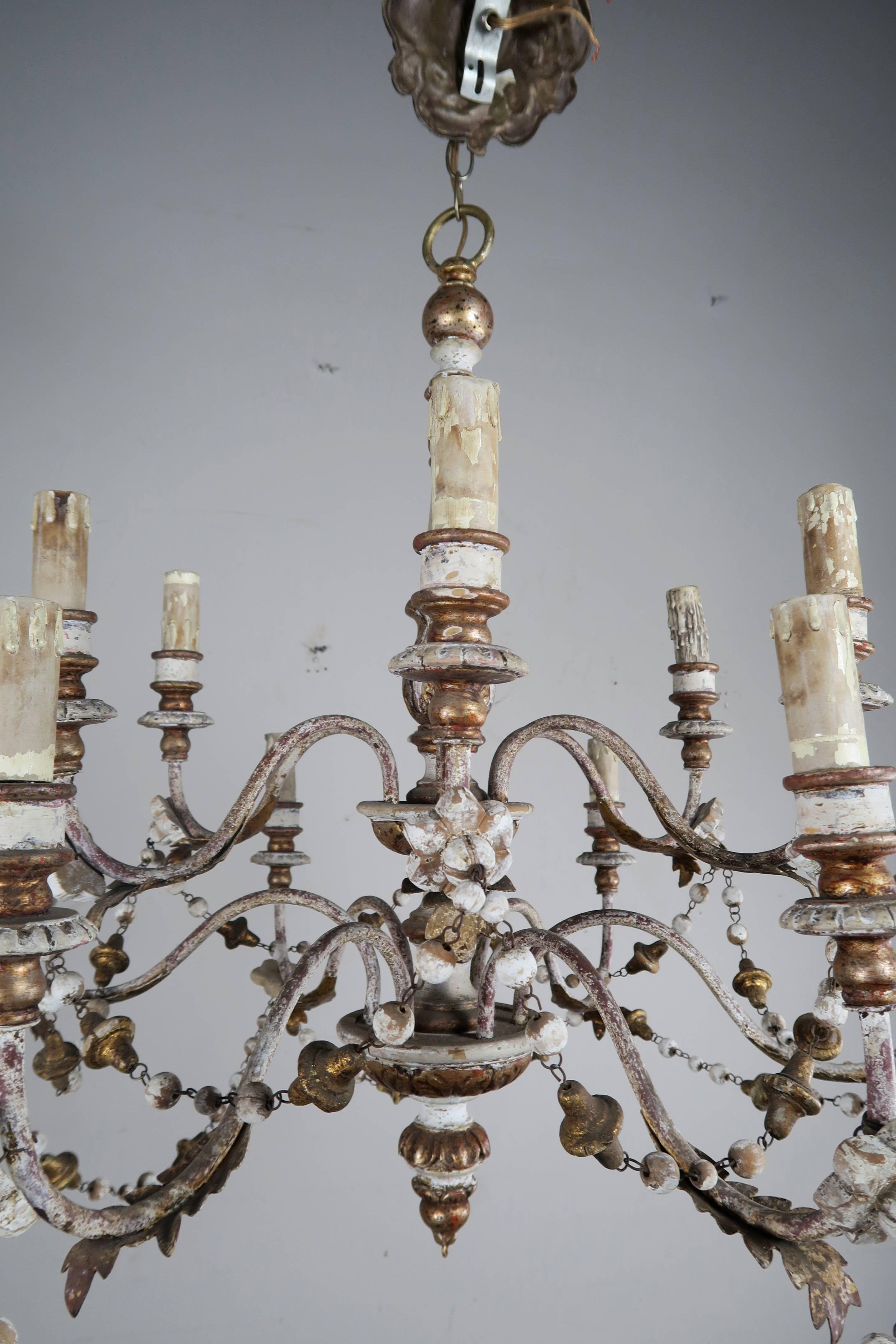 Twelve-light wood beaded white painted and parcel-gilt chandelier. The fixture is adorned with garlands of wood beads. The fixture is in working condition and ready to install.