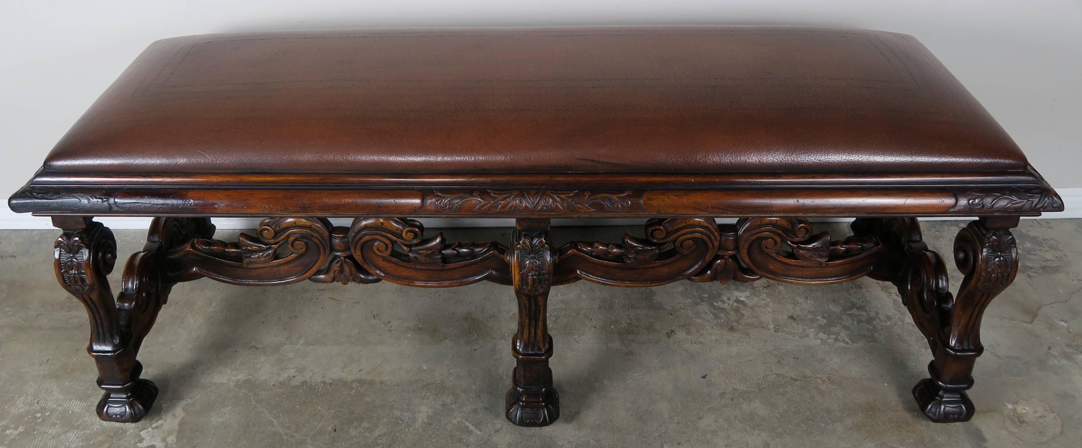 Six-legged carved English walnut embossed leather bench with floral vine detail on the corners and flowers at the top of each leg. All legs meet at beautifully carved center stretcher.