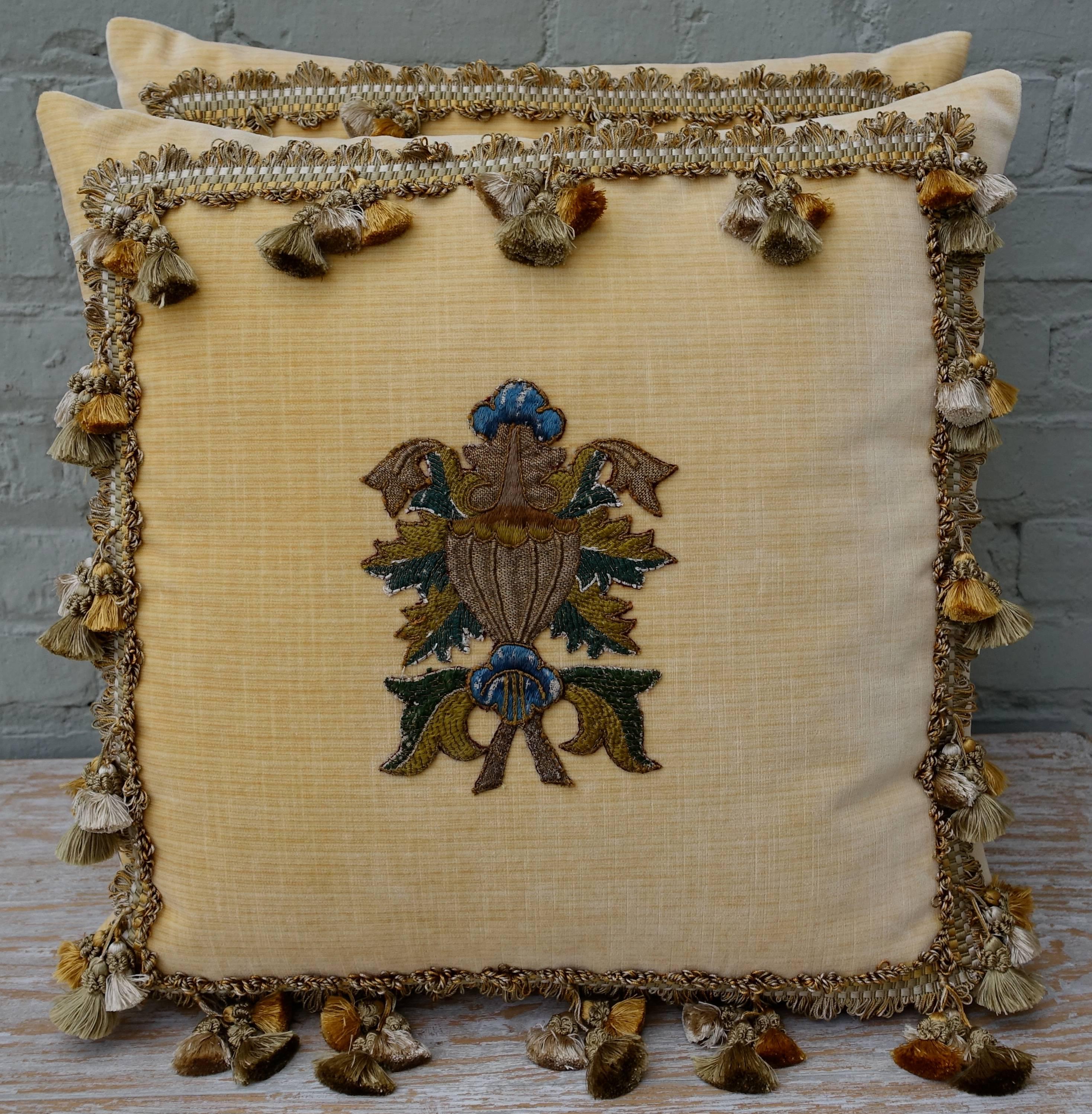 A pair of yellow velvet pillows with 18th century metallic gold and silk urn applique and tricolor silk tassel fringe detail. Linen backs, down inserts and sewn closed.