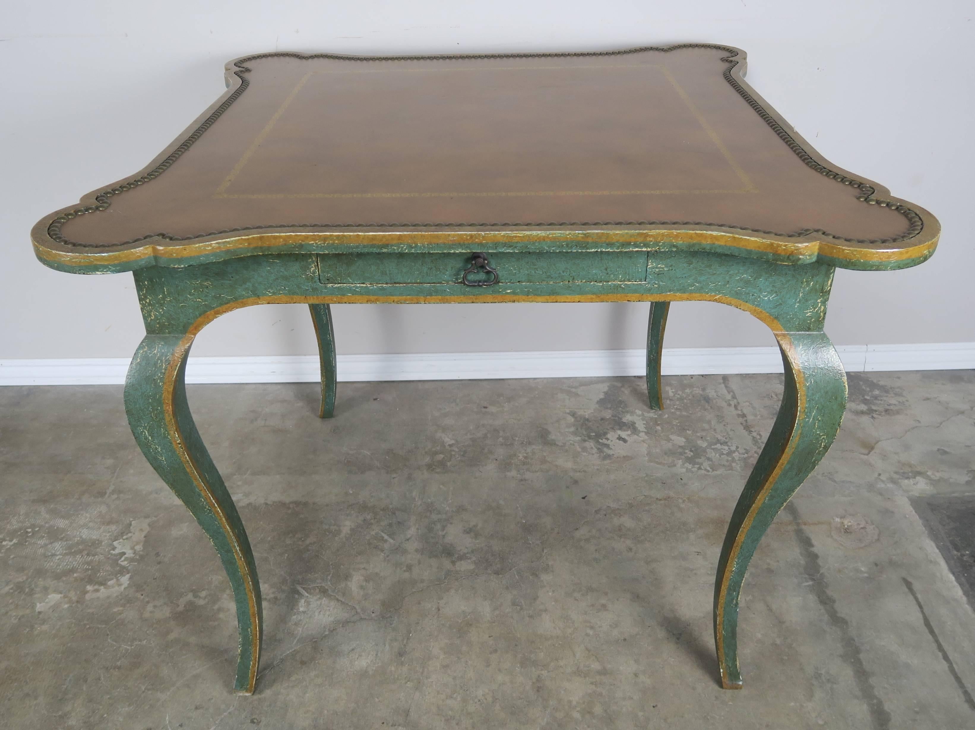 Painted French style game table with embossed leather top by Minton-Spidell. The table is painted green and gold and stands on four cabriole legs with a single drawer. The top is a caramel colored leather with nailhead trim detail and gold embossing.