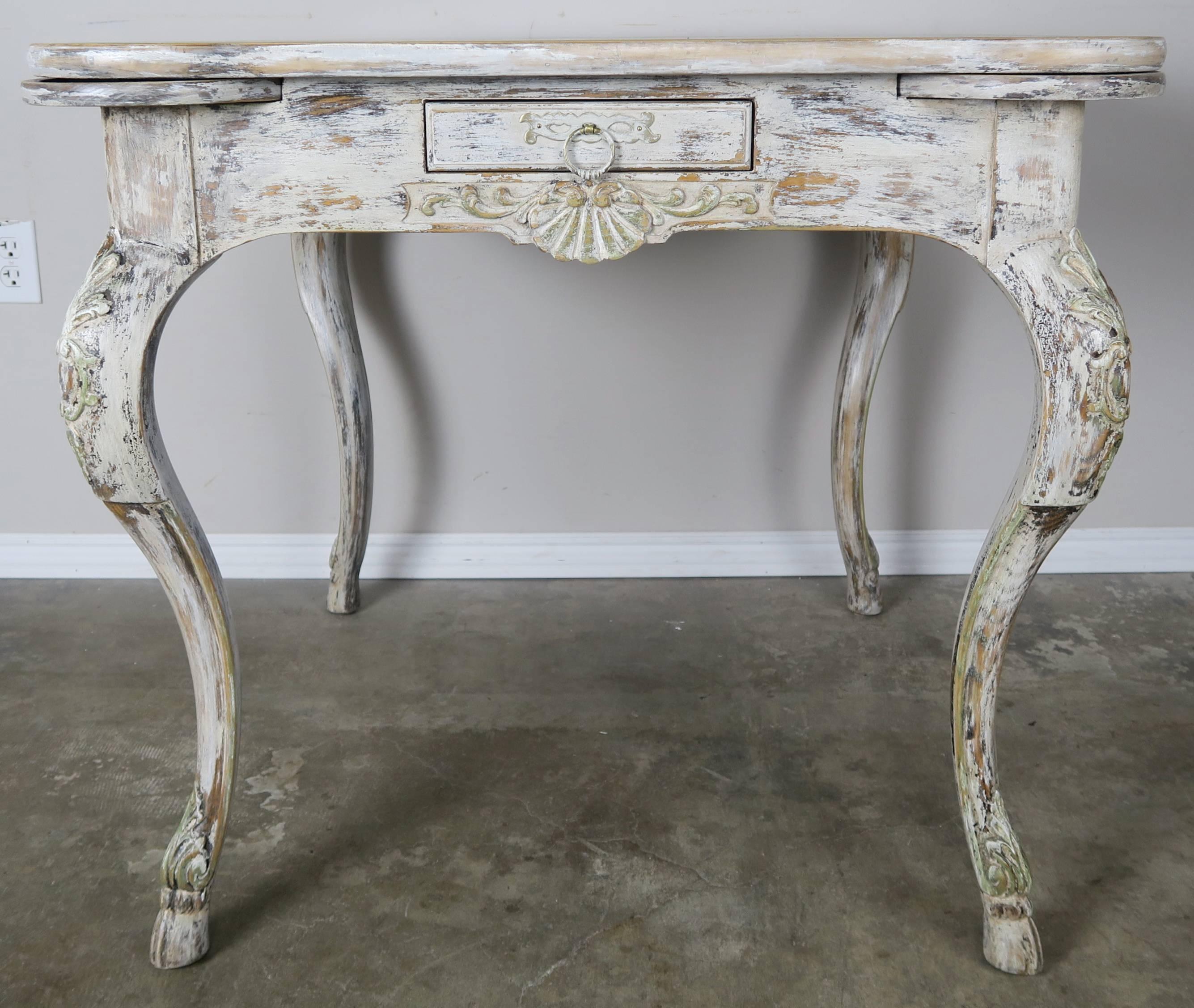 French painted game table with weathered finish. Each corner has a  circular pull out shelf for drinks.  Single drawer with pull out ring and surrounding hardware. The table stands on four carved cabriole legs that end in animal hoof feet.  Carved
